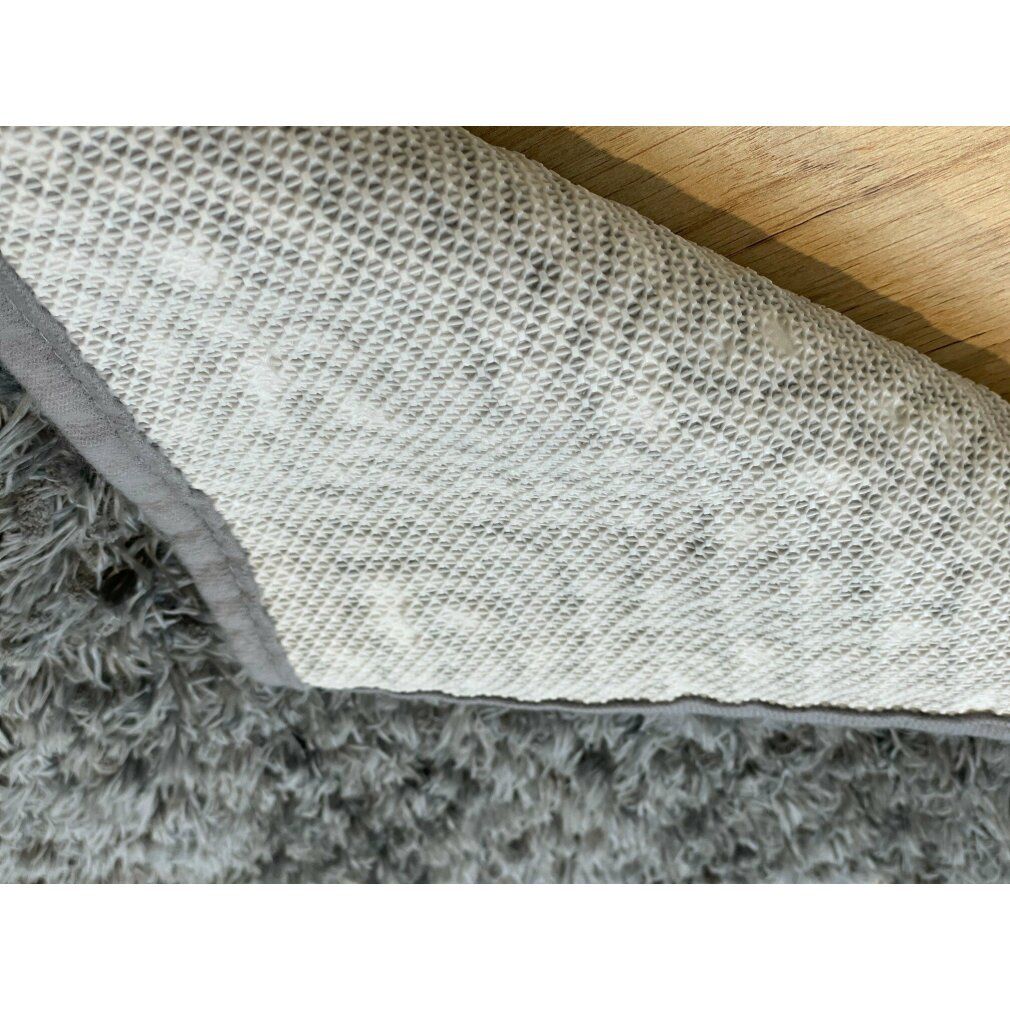 Royal Dry Doormat m, Unterseite. Grauer, flauschiger Teppich mit weißer, strukturierter Unterseite. Holzuntergrund.