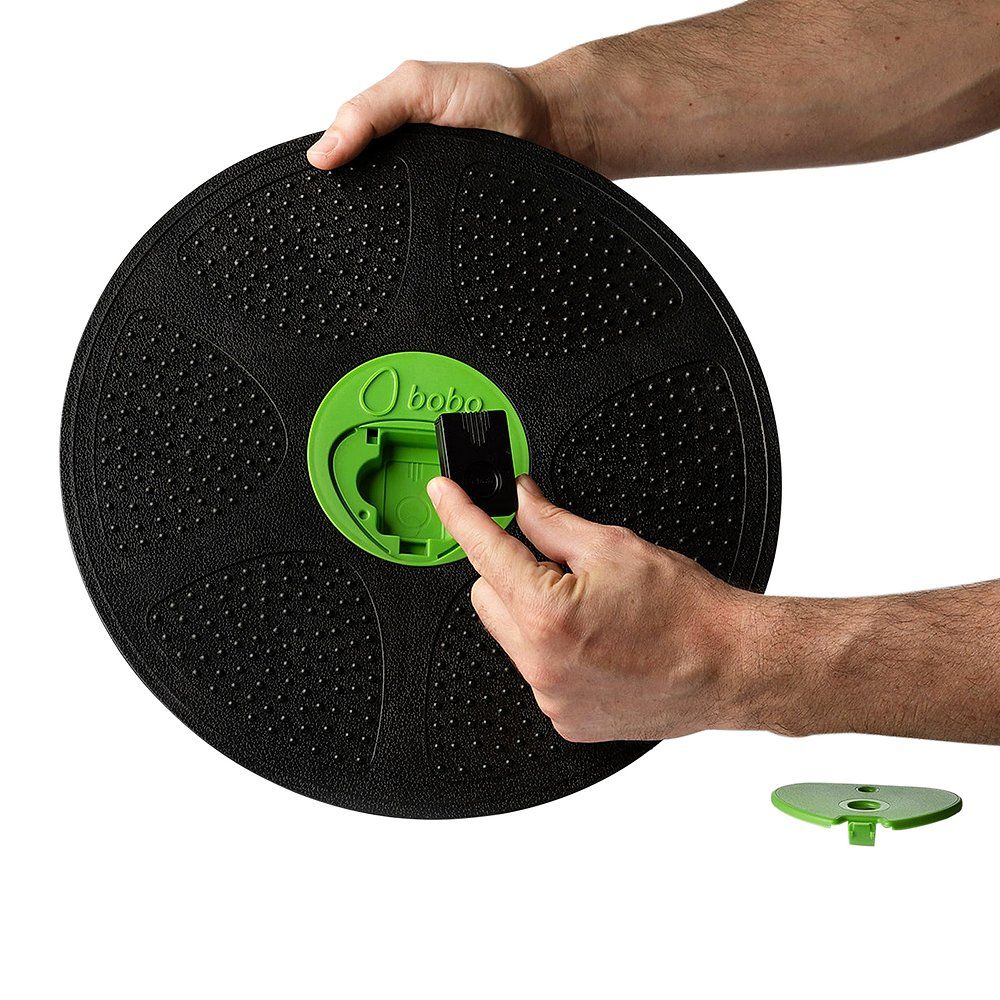Hände halten einen schwarzen Einsatz für das Balance Board. Grünes Board mit Logo.