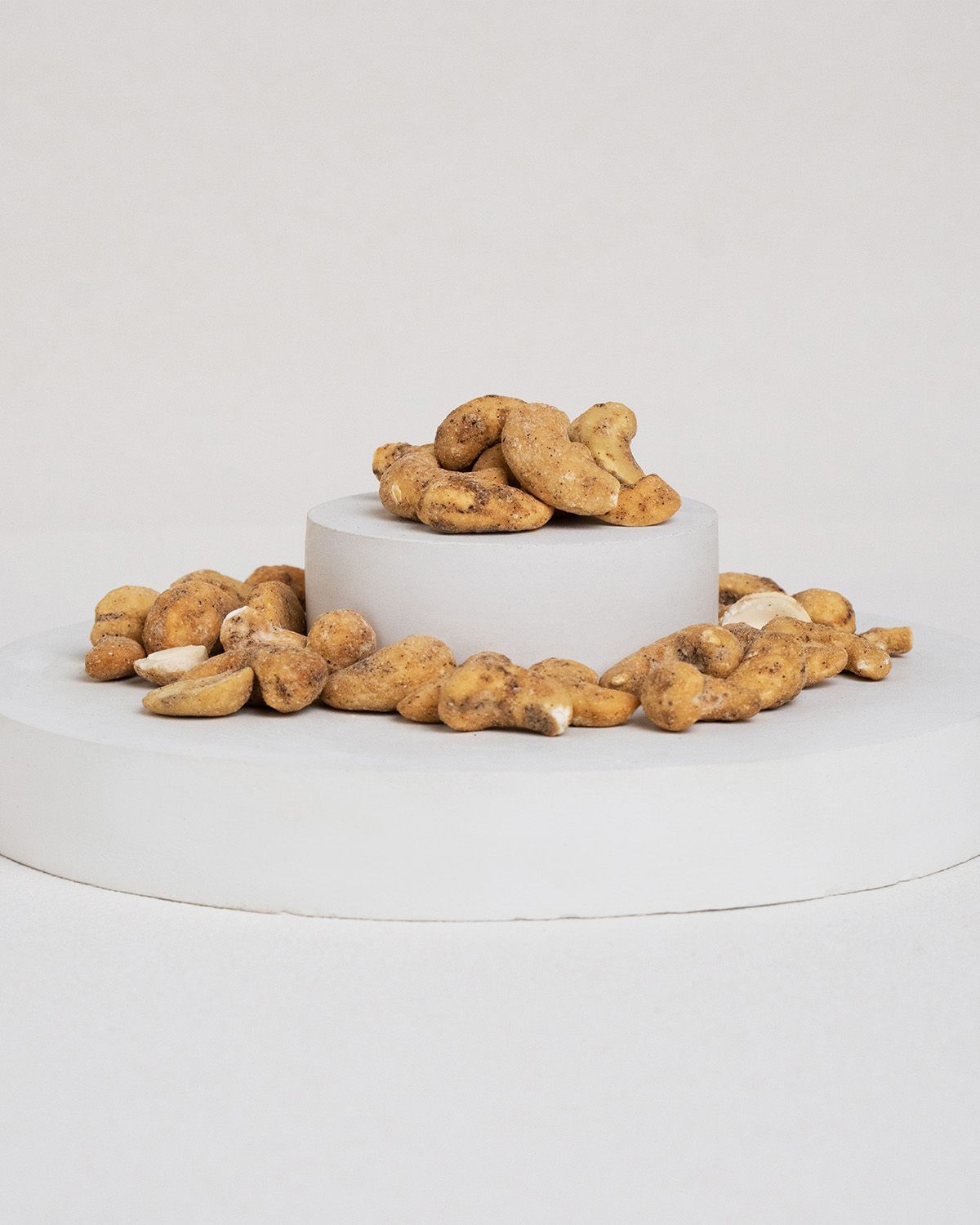 Cashewkerne auf einem weißen Podest. Einige Kerne liegen um das Podest herum.