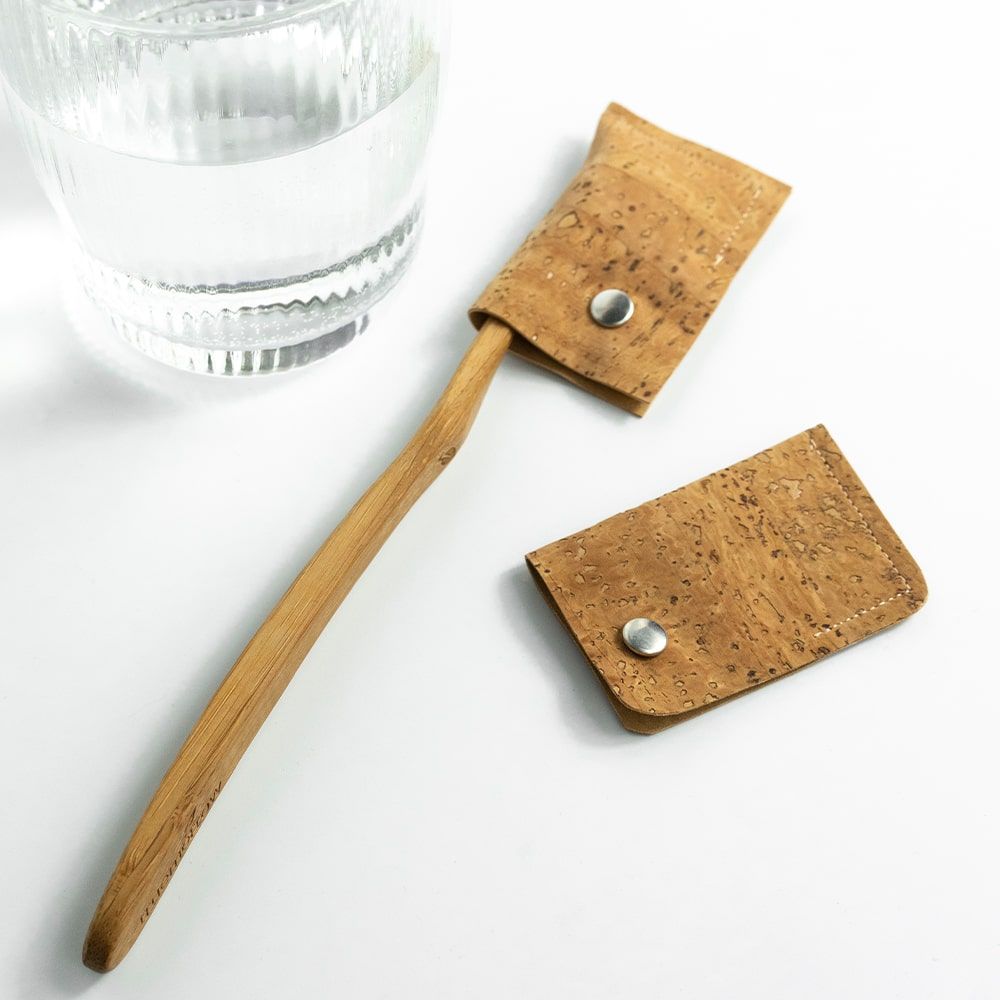 Zahnbürsten-Schutzhülle aus Kork. Hellbraun, mit Druckknopf. Neben einer Holzzahnbürste und einem Glas Wasser.