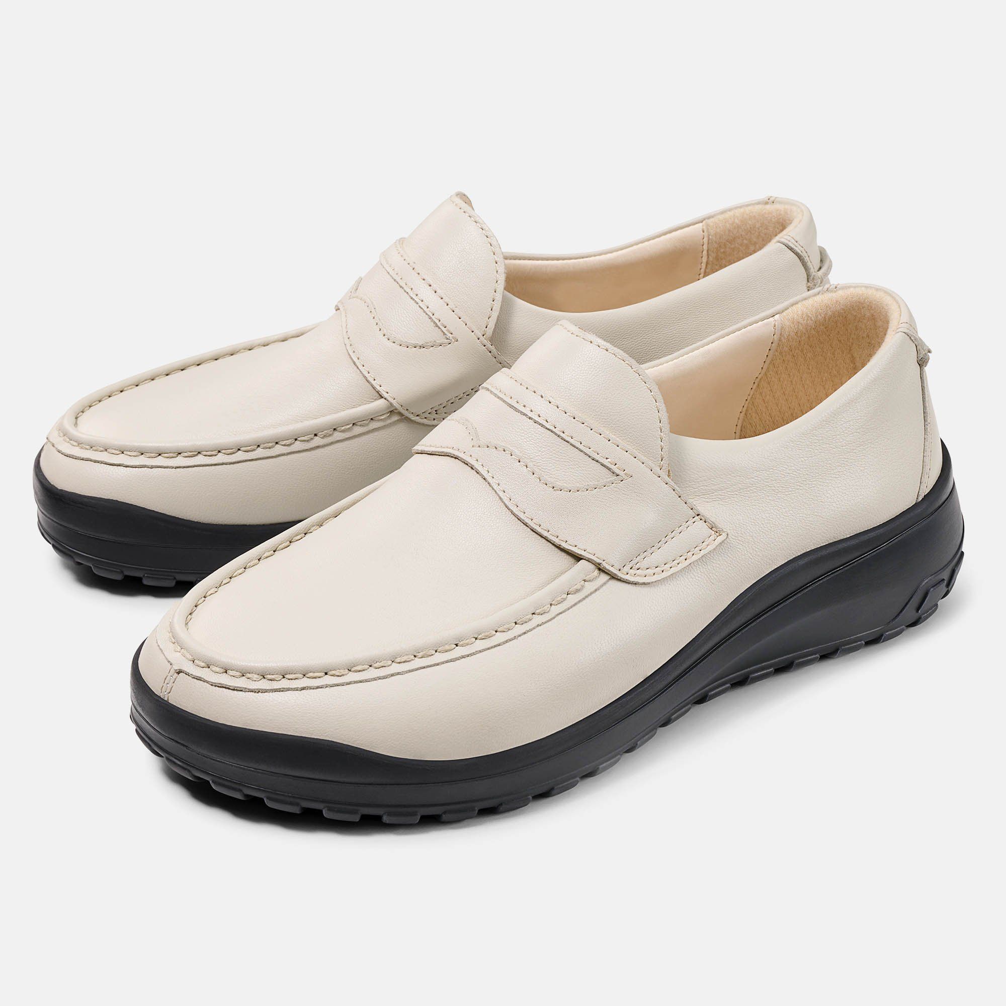 Zwei cremefarbene Slipper mit schwarzer Sohle. Klassisches Design mit Ziernaht und Riemen. Breiter Schnitt.