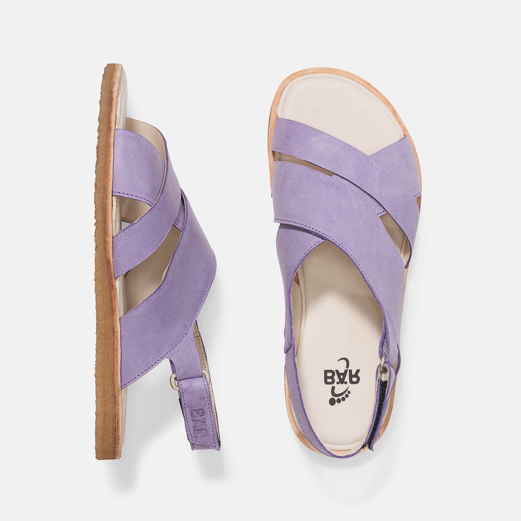 Zwei Sandalen, eine von oben, eine von der Seite. Violett mit gekreuzten Riemen. Beige Innensohle, braune Sohle. BÄR-Logo.