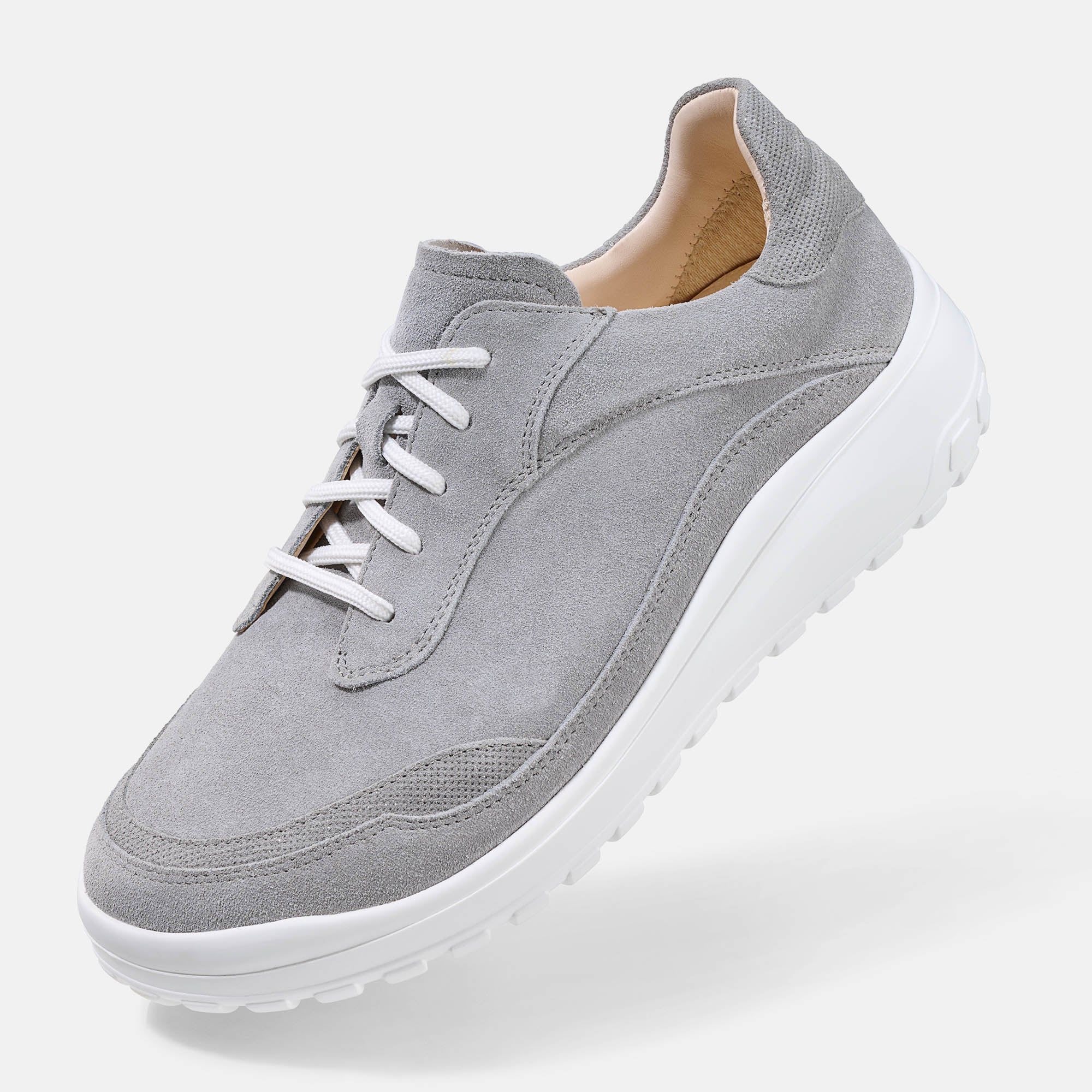 Grauer Schnürschuh mit weißer Sohle. Breiter Schnitt. Hellgraues Wildleder-Obermaterial. Weiße Schnürsenkel. Schuh von der Seite.