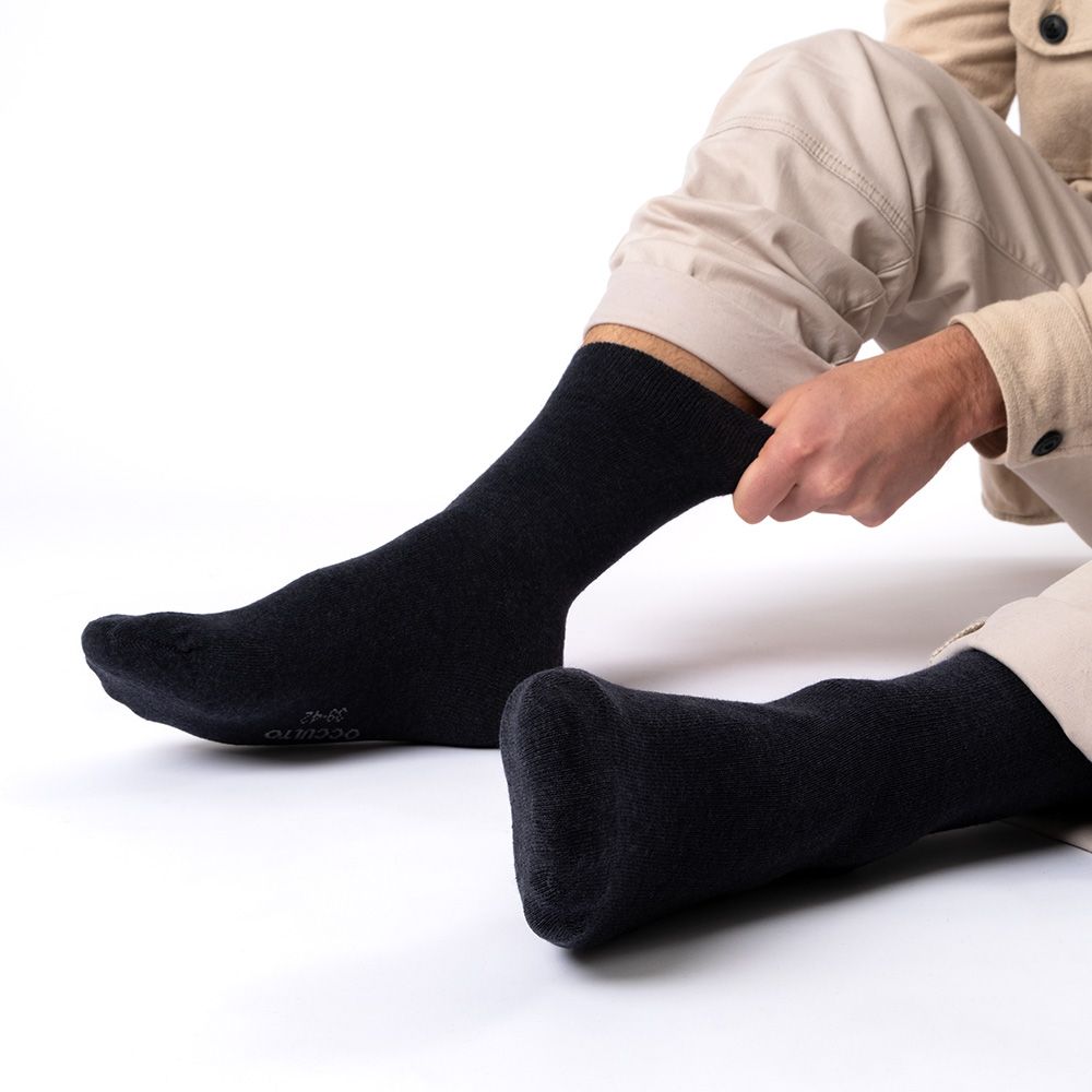 Schwarze Socken, ohne Gummibund, werden von einer Person angezogen. Baumwolle. Person sitzt.