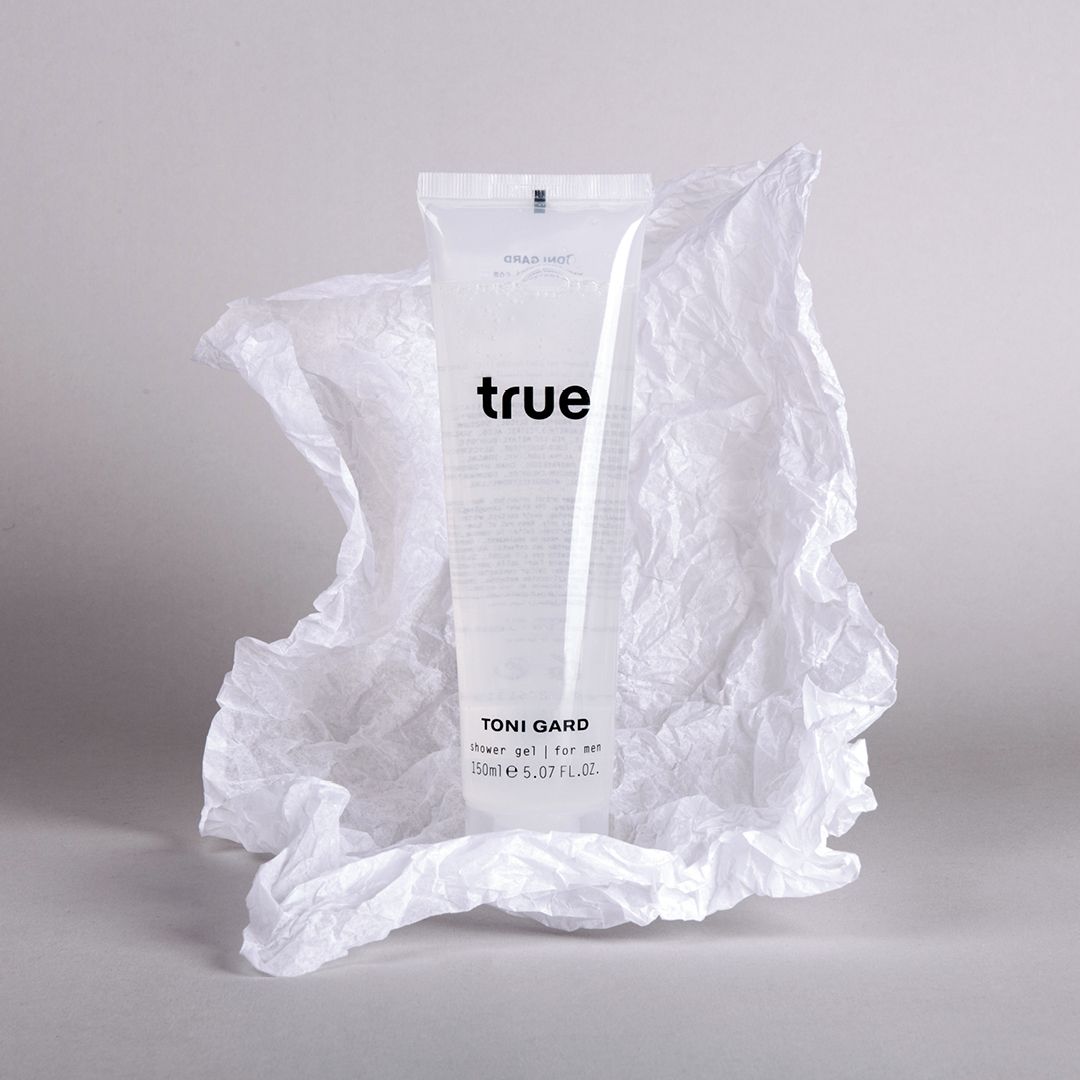Transparente Tube mit "true"-Schriftzug und "TONI GARD"-Logo, umhüllt von zerknittertem, weißem Papier. Duschgel für Männer.