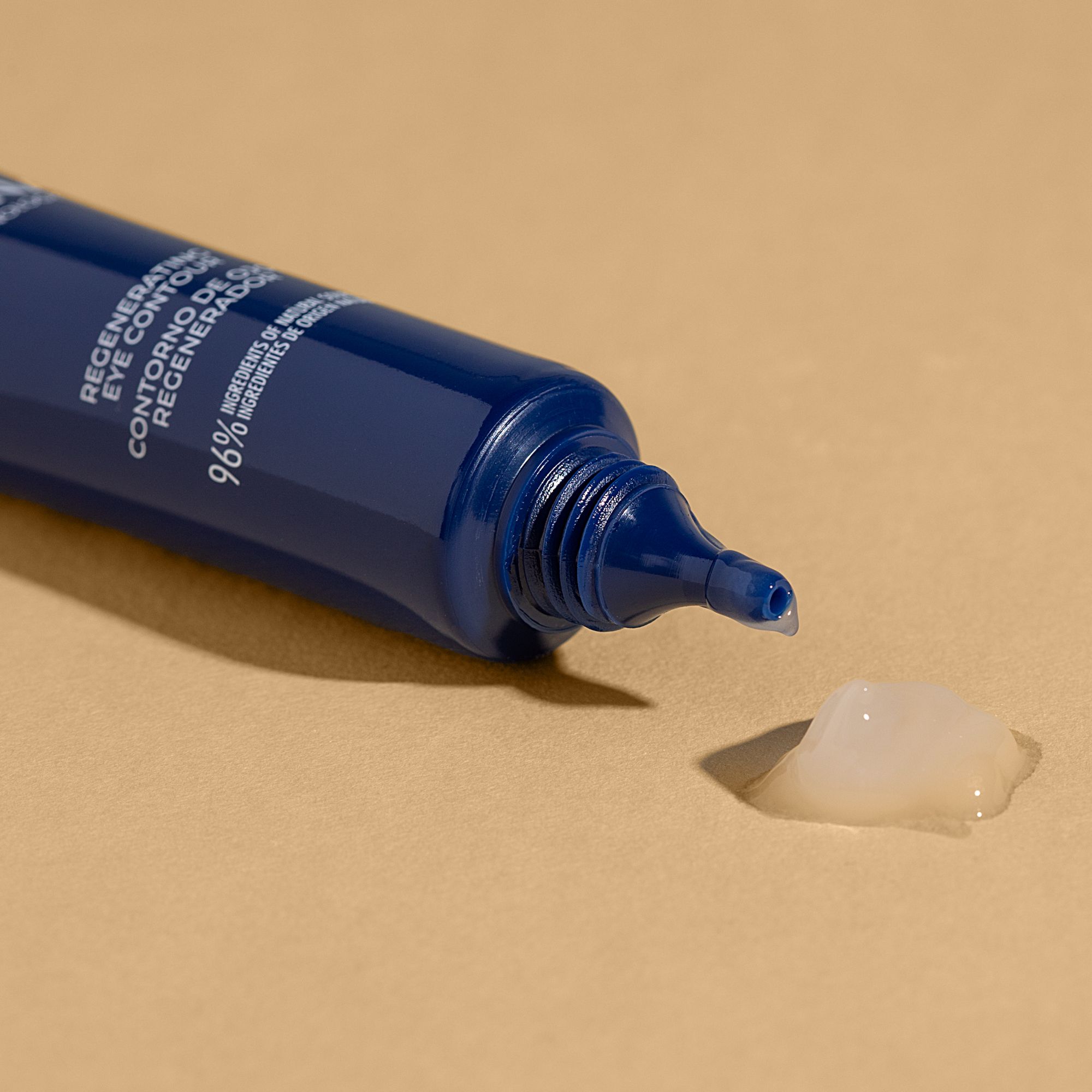 Dunkelblaue Tube, Produkt wird herausgedrückt. Aufschrift: Regenerating Eye Contour. 96% Inhaltsstoffe natürlichen Ursprungs. Gel auf beigem Untergrund.