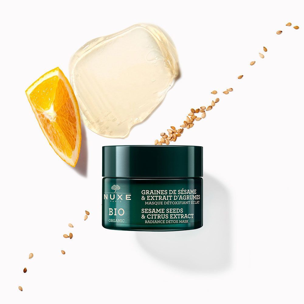 NUXE BIO-Gesichtsmaske mit Zutaten: Orangenscheibe, Sesamkörner und Maskenprobe. Text: GRAINES DE SÉSAME & EXTRAIT D'AGRUMES, MASQUE DÉTOXIFIANT ÉCLAT, RADIANCE DETOX MASK.