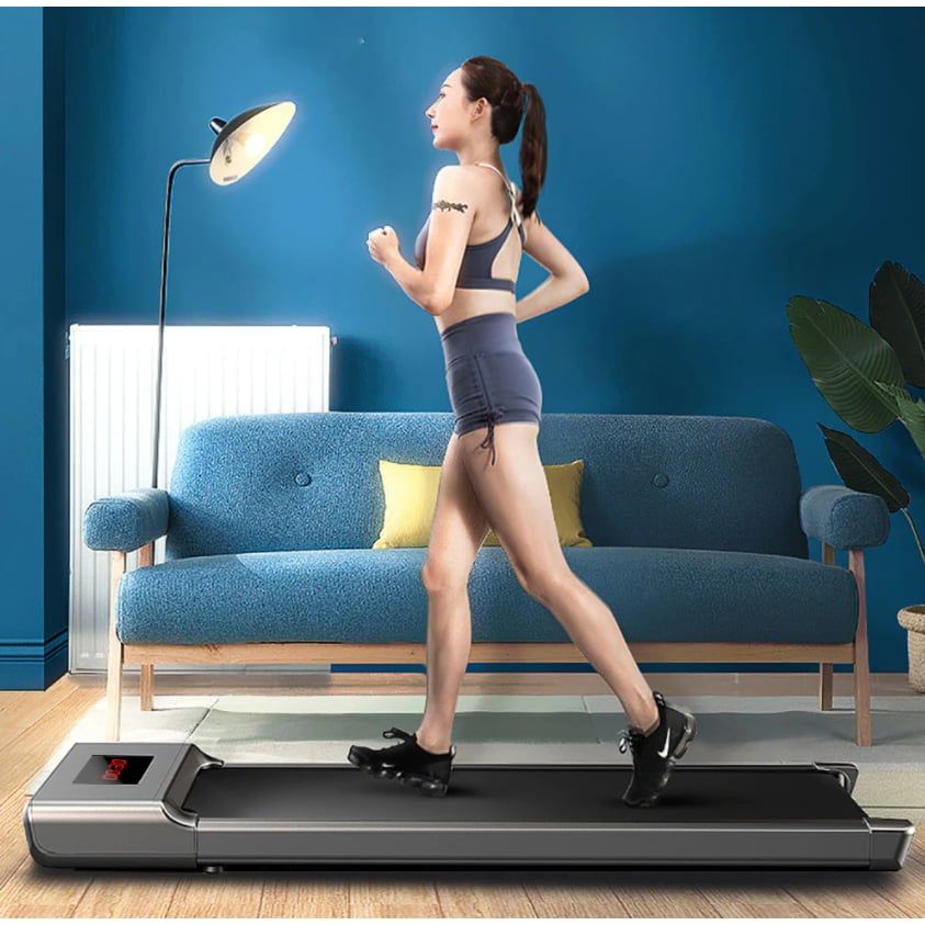 Frau läuft auf einem Laufband. LED-Display sichtbar. Hintergrund: Sofa, Lampe.