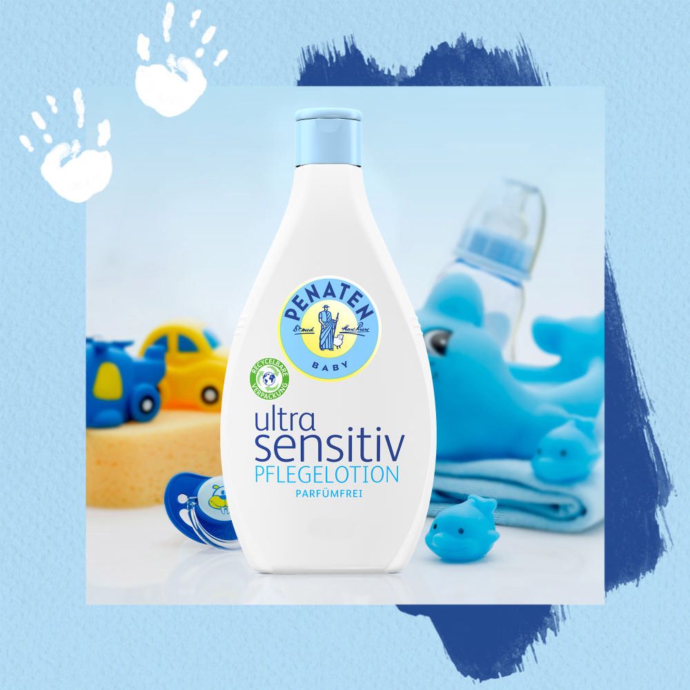 Weiße Flasche mit blauem Deckel. Aufschrift: Ultra Sensitiv Pflegelotion, parfümfrei. Logo: Penaten Baby. Spielzeug im Hintergrund.