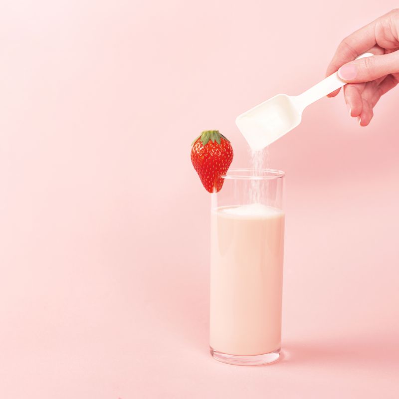 Glas mit rosa Flüssigkeit, Erdbeere, Löffel mit Pulver, Hand. Rosa Hintergrund.