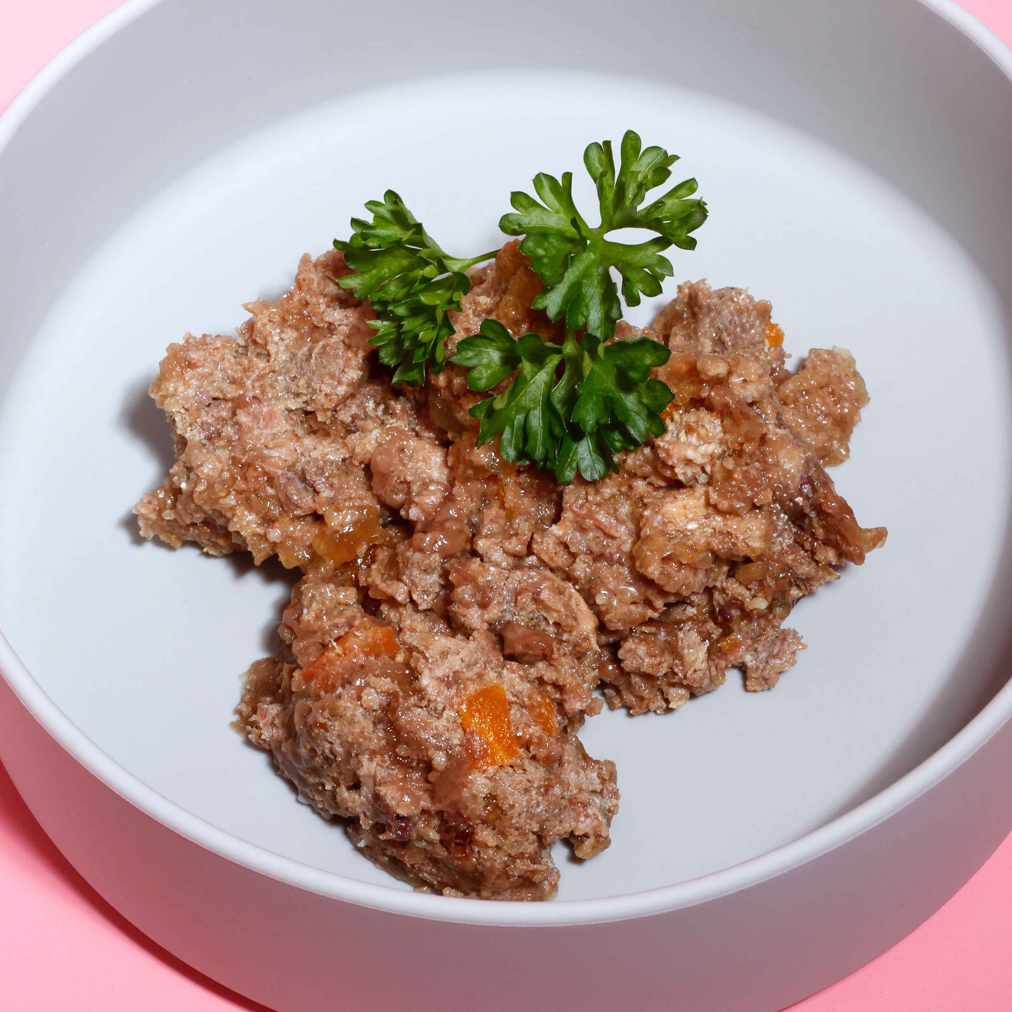 Hundefutter in einer weißen Schüssel. Das Futter ist grob zerkleinert und mit Petersilie garniert.