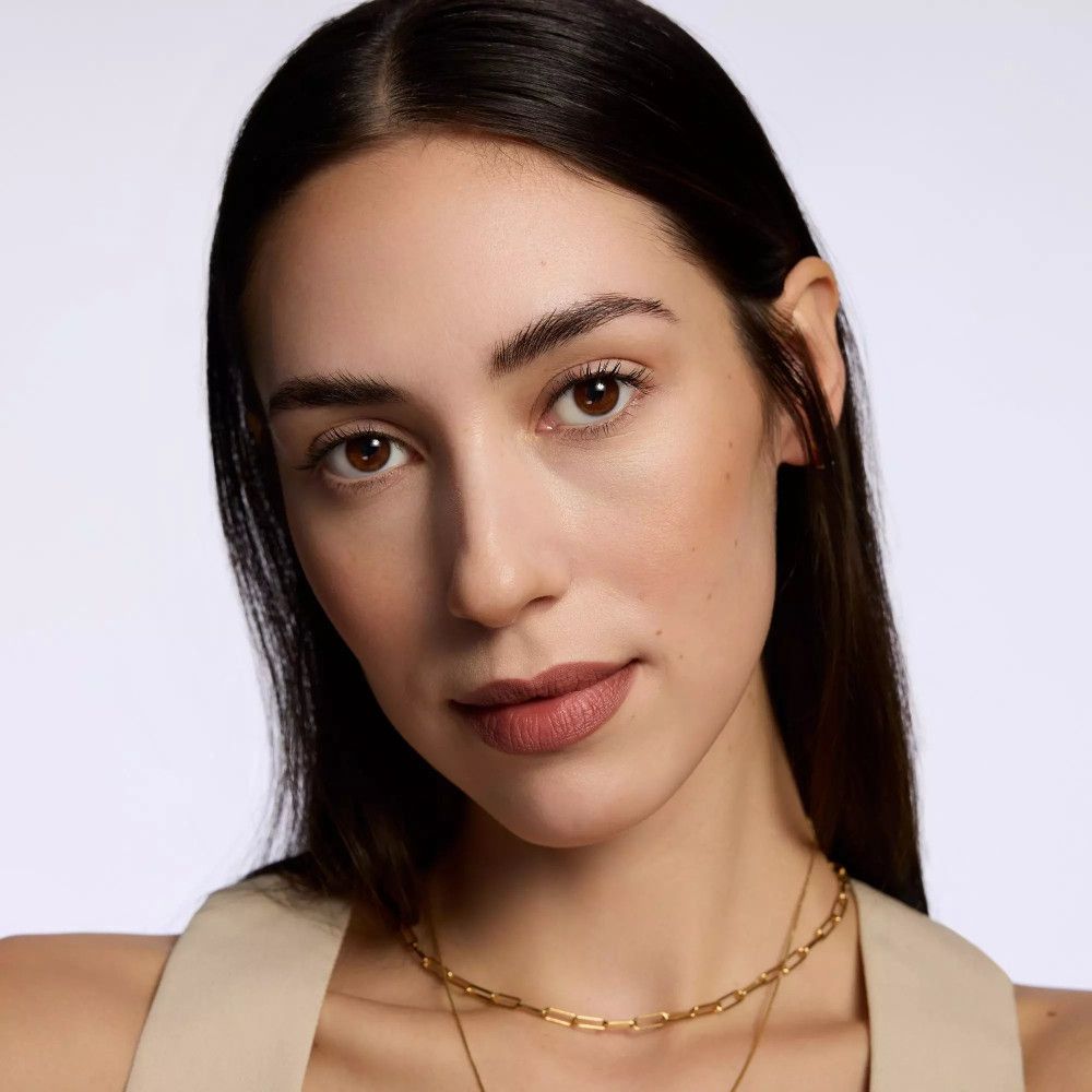 Porträt einer Frau mit braunen Lippen. Sie trägt eine goldene Halskette.