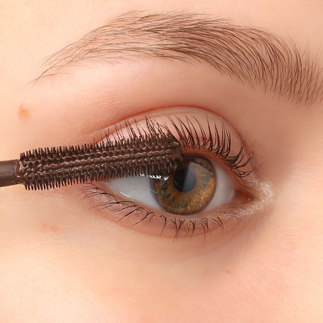 Auge mit Wimperntusche. Die Mascarabürste wird auf die Wimpern aufgetragen.
