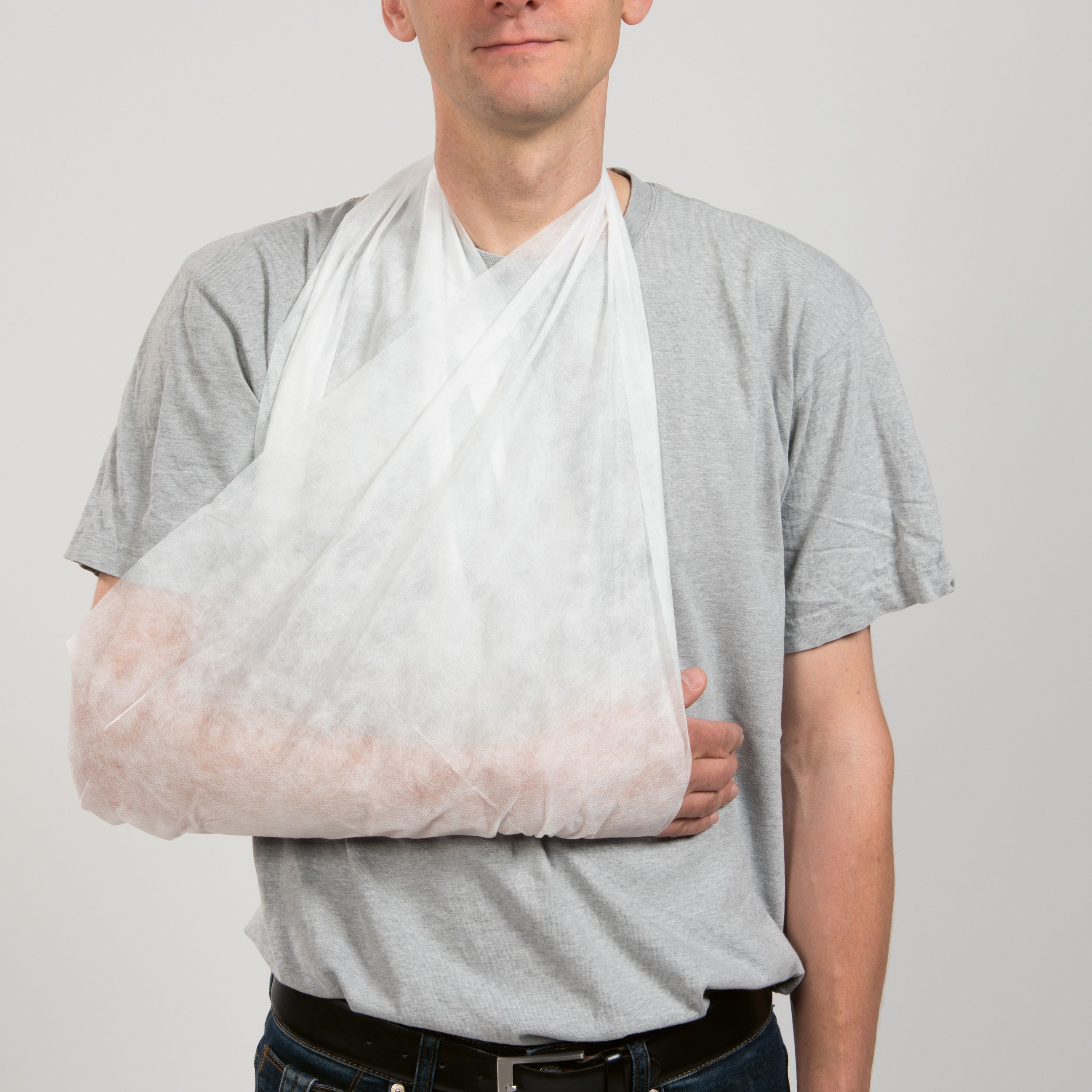 Person mit weißem Dreiecktuch am Arm. Das Tuch stützt den Arm. Der Mann trägt ein graues T-Shirt.