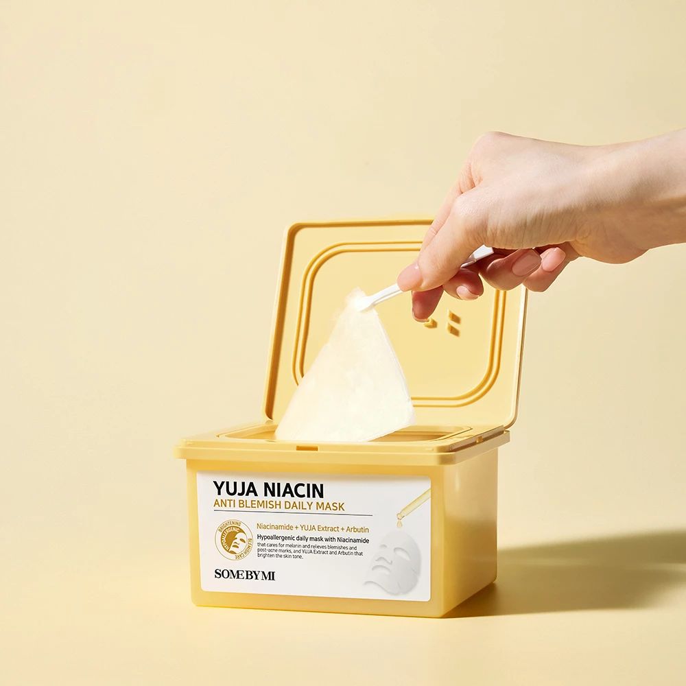 Geöffnete gelbe Maskenpackung. Hand entnimmt eine Gesichtsmaske. Aufschrift: Yuja Niacin Anti Blemish Daily Mask.