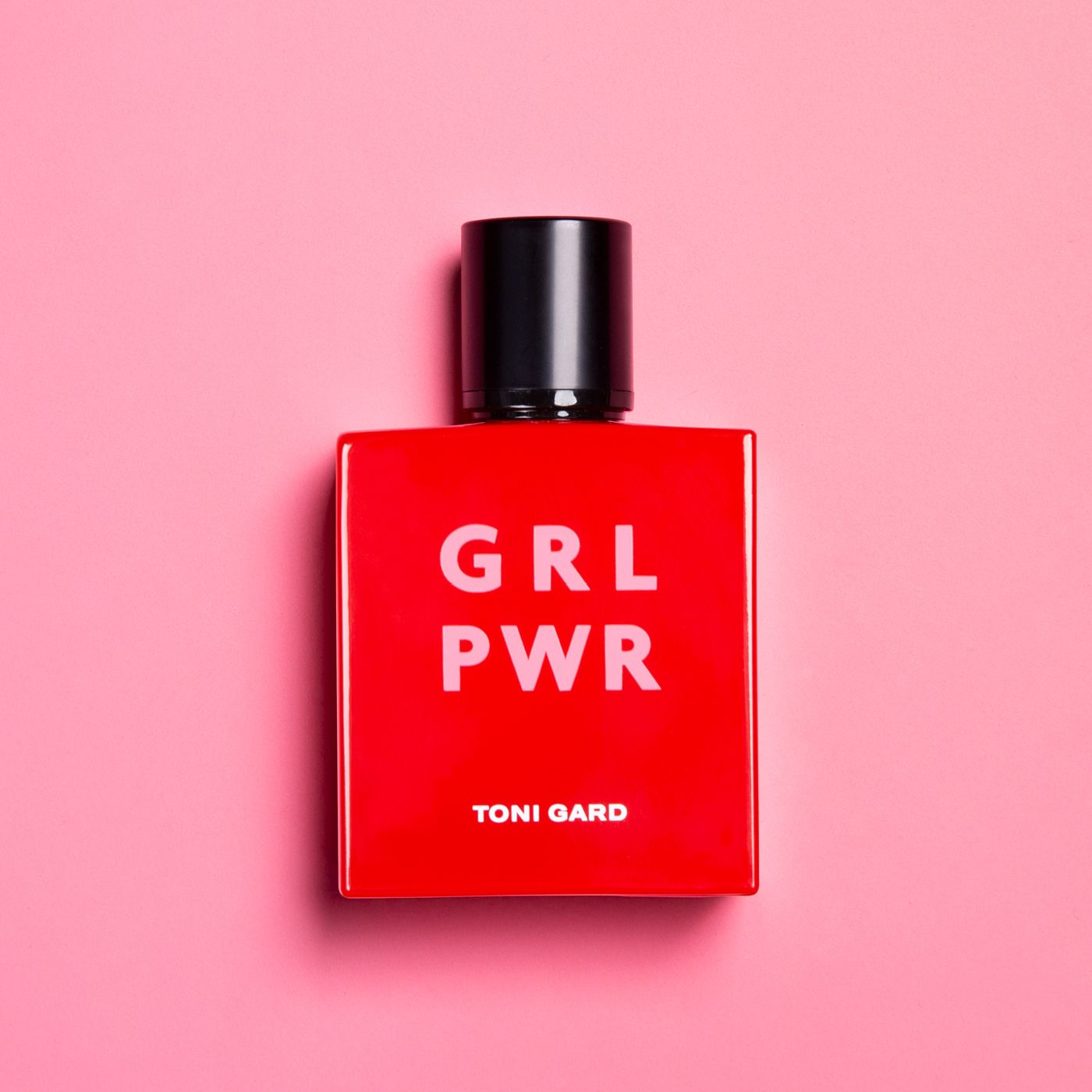 Rote rechteckige Flasche mit schwarzem Verschluss. Text: GRL PWR, TONI GARD. Rosa Hintergrund.
