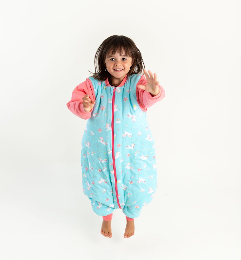 Kind springt in türkisblauem Schlafsack mit Einhorn-Muster. Roter Reißverschluss und Ärmel. Füße mit rotem Bündchen. Oeko-Tex Qualität.