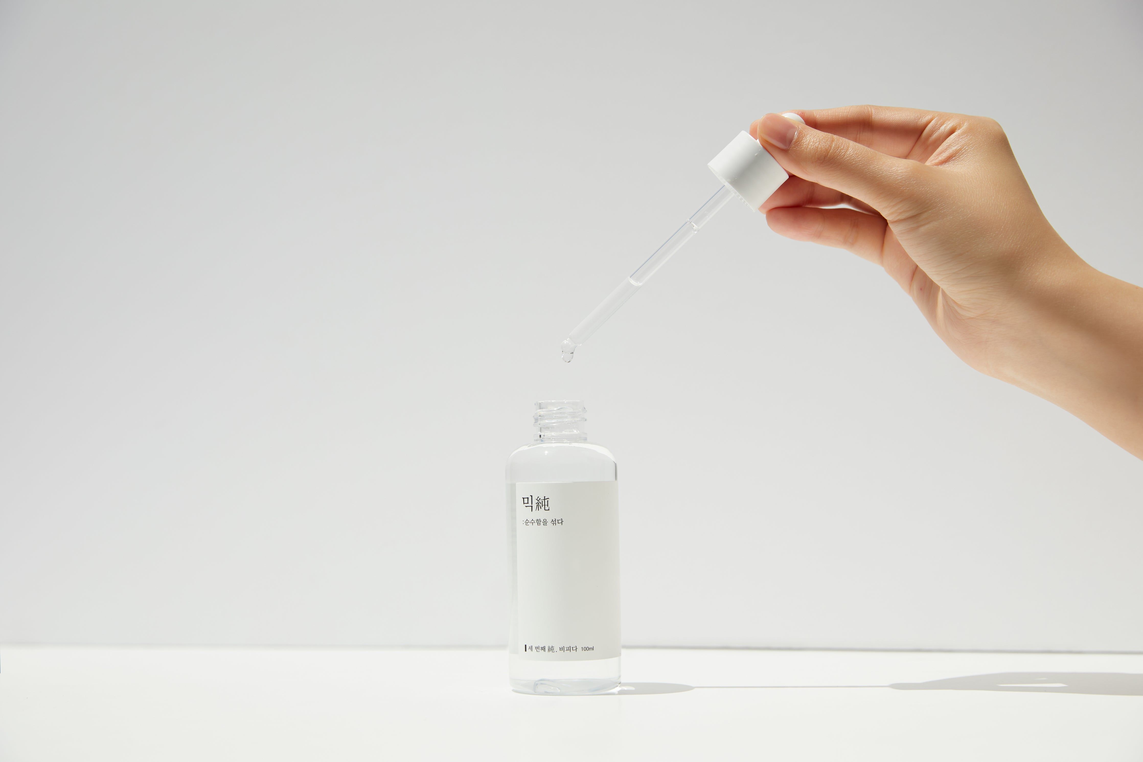 Transparente Flasche mit Tropfer. Hand hält Tropfer über der Flasche. Tropfen fallen in die Flasche.