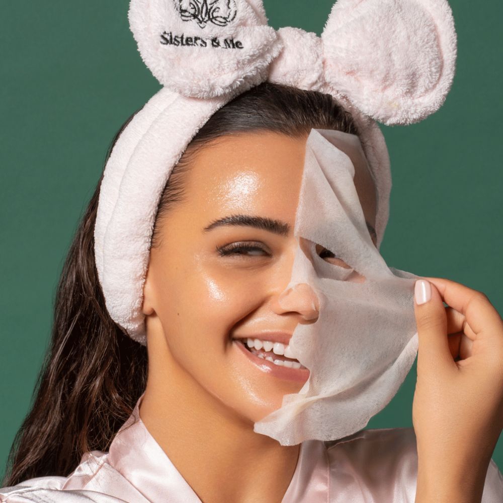 Frau mit Gesichtsmaske und Haarband. Maske wird von Gesicht abgezogen. Haut glänzt.