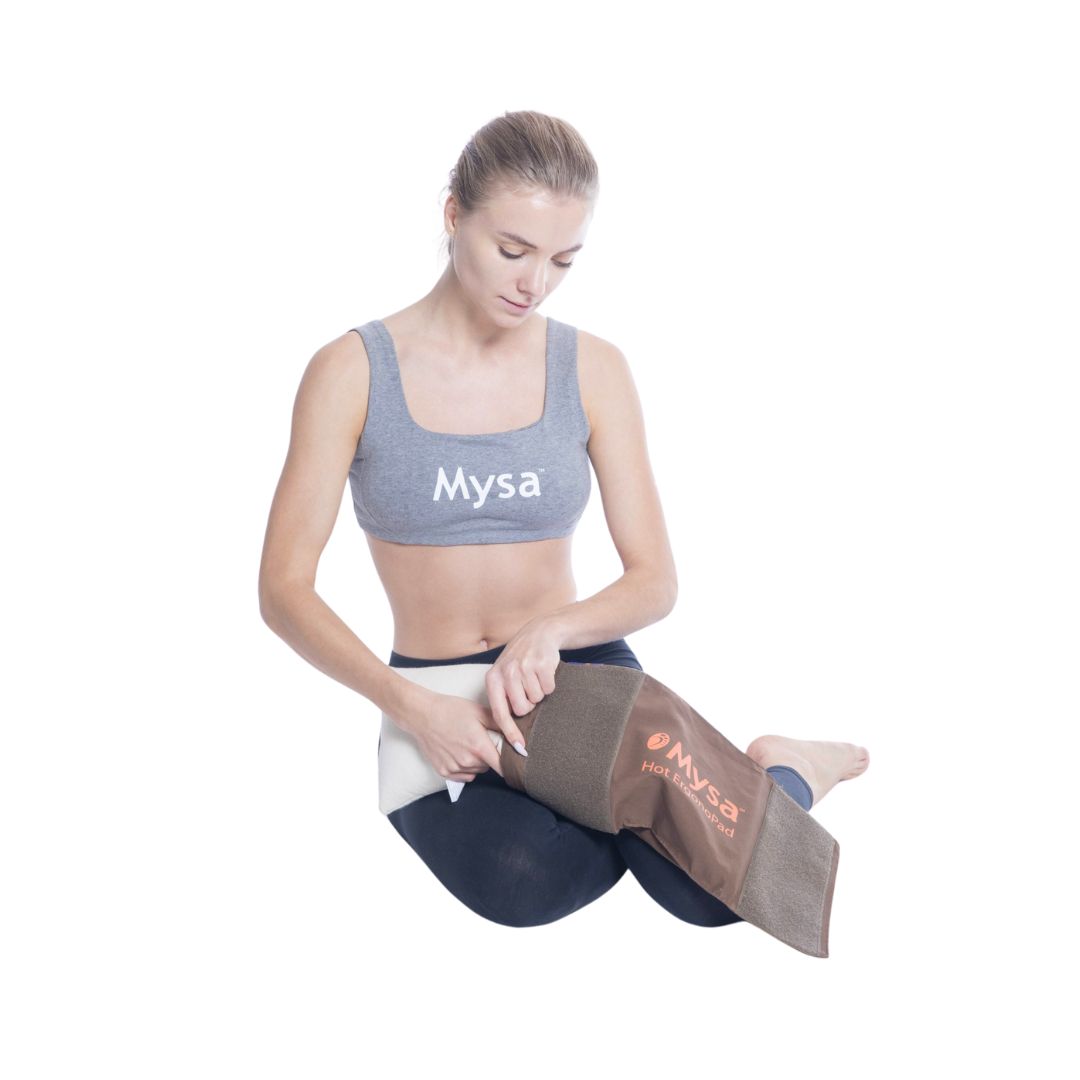 Frau sitzt und hält ein braunes Kissen. Das Kissen hat das Mysa-Logo. Sie trägt Sportkleidung.