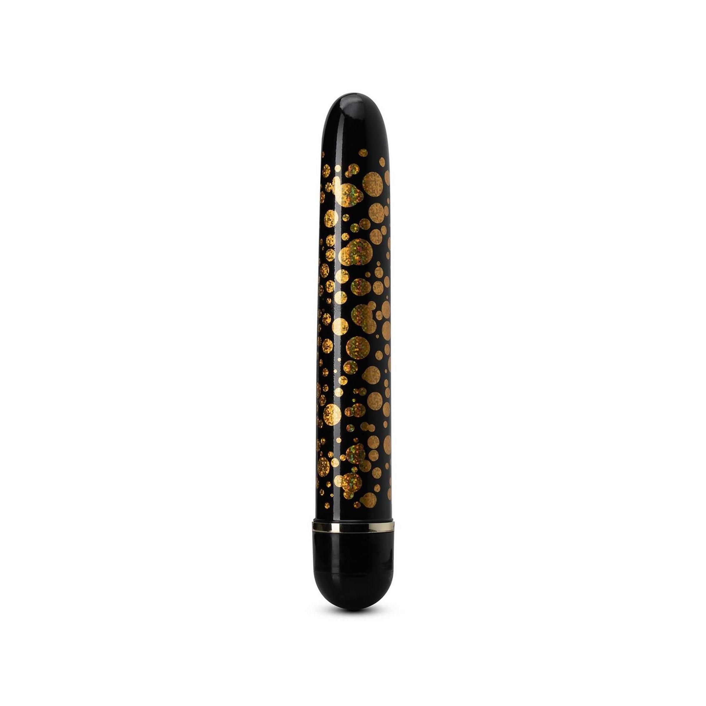 Schwarzer Vibrator mit goldenen Punkten. Zylindrische Form, abgerundete Enden. Schwarzer Sockel.