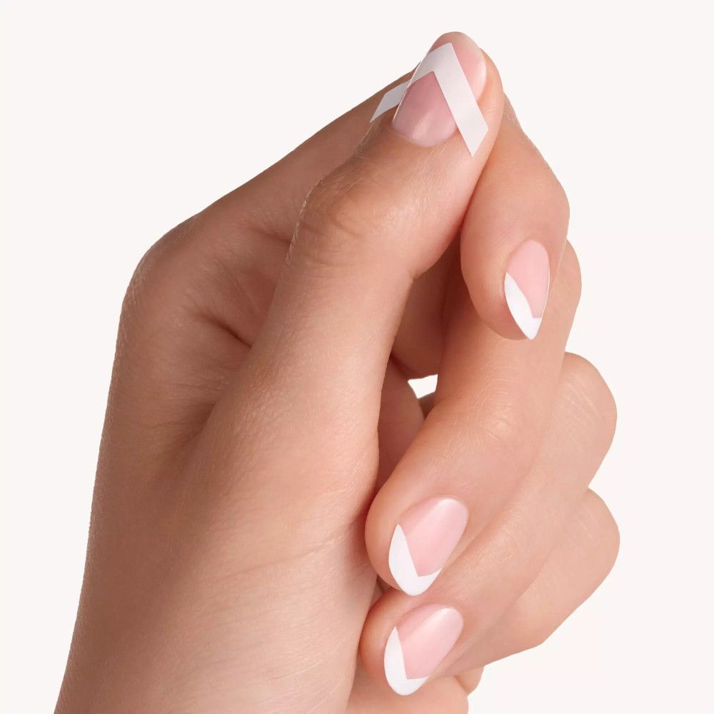 Hand mit French Manicure. Ein Finger mit Schablone. Die Nägel sind mit weißem Nagellack lackiert.