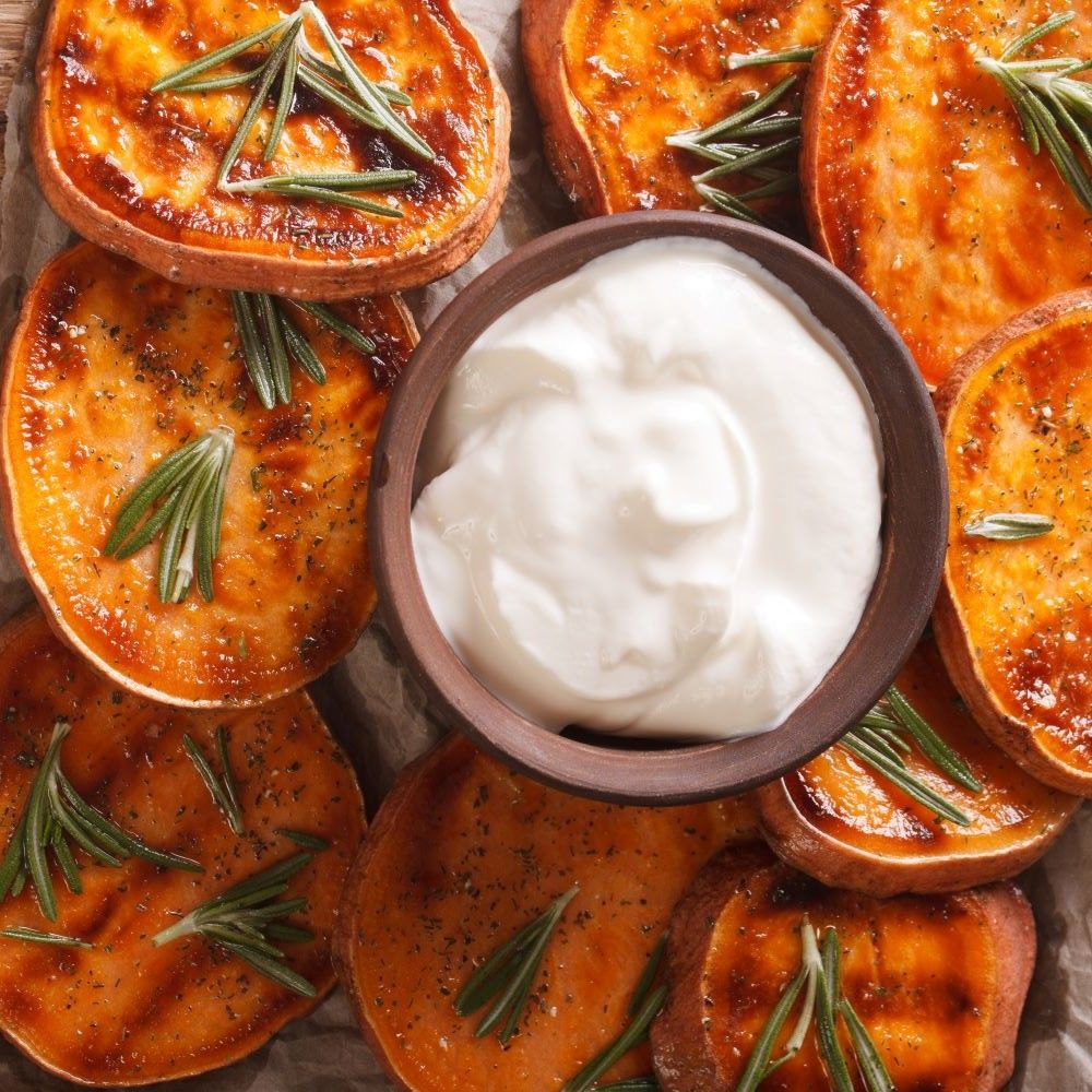 Gebratene Süßkartoffelscheiben mit Rosmarinzweigen und Schale mit weißer Creme.