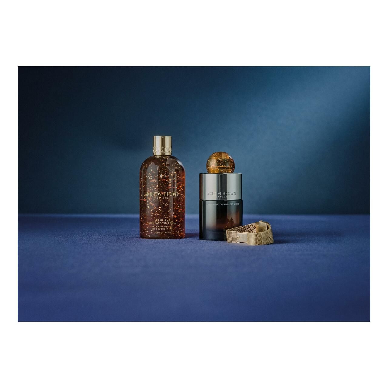 Zwei Flakons und ein goldfarbener Verschluss auf blauem Untergrund. Produkte: Molton Brown, Mesmerising Oudh Accord & Gold.