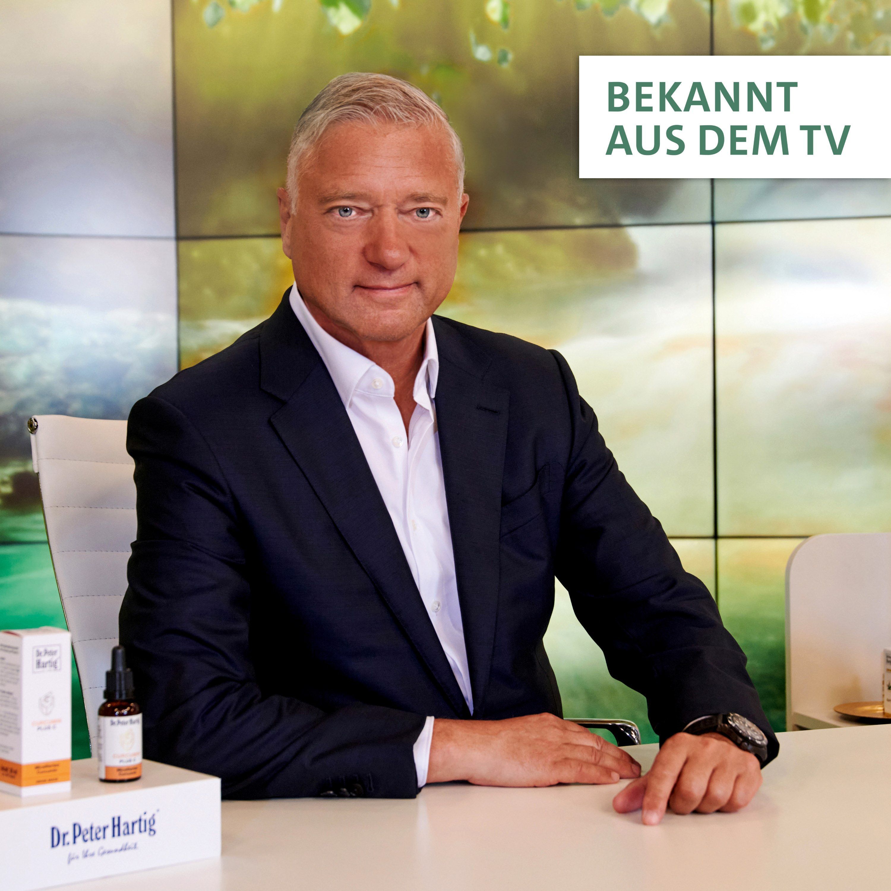 Mann im Anzug sitzt an einem Tisch. Auf dem Tisch: Produktverpackung und Flasche. Text: Bekannt aus dem TV.