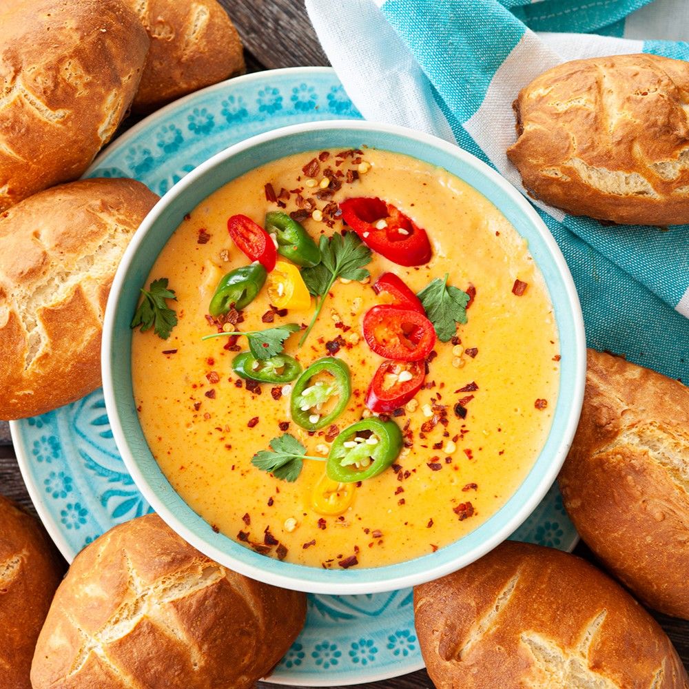 Schüssel mit gelber Suppe, garniert mit Chili und Kräutern. Brotstücke um die Schüssel herum. Türkis-farbener Teller.