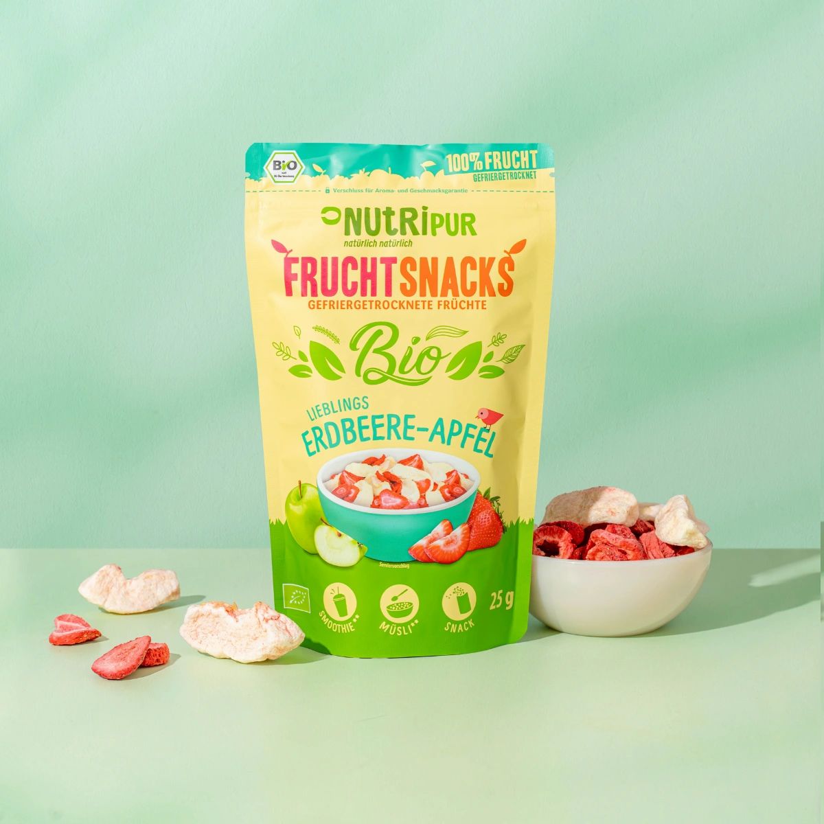 Beutel mit gefriergetrockneten Erdbeere-Apfel-Früchten. Daneben Schale mit Früchten und lose Früchte. Bio-Siegel und 100% Frucht-Logo.