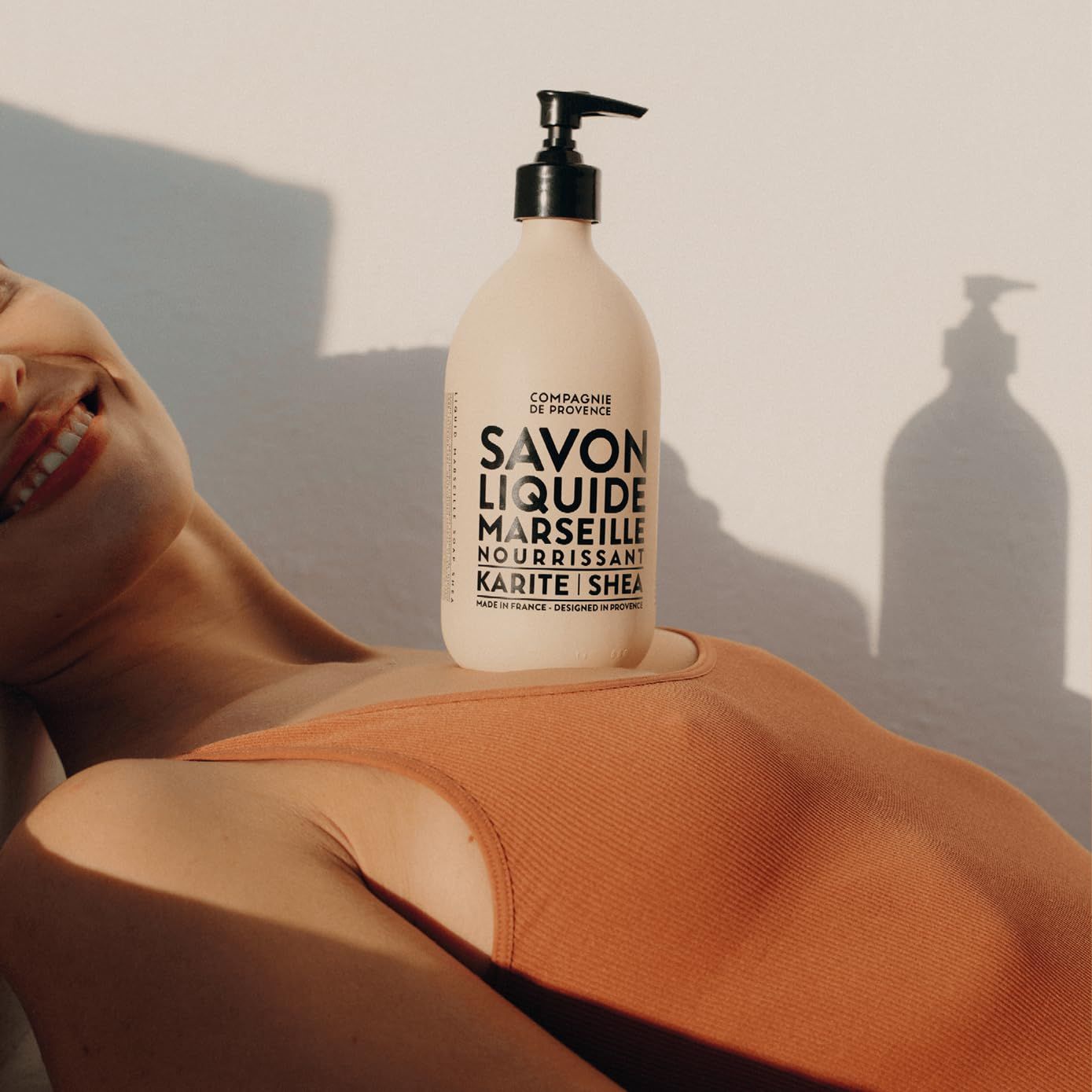 Frau liegt mit Produkt auf der Brust. Flasche mit schwarzem Pumpkopf. Text: Savon Liquide Marseille, Karité/Shea.