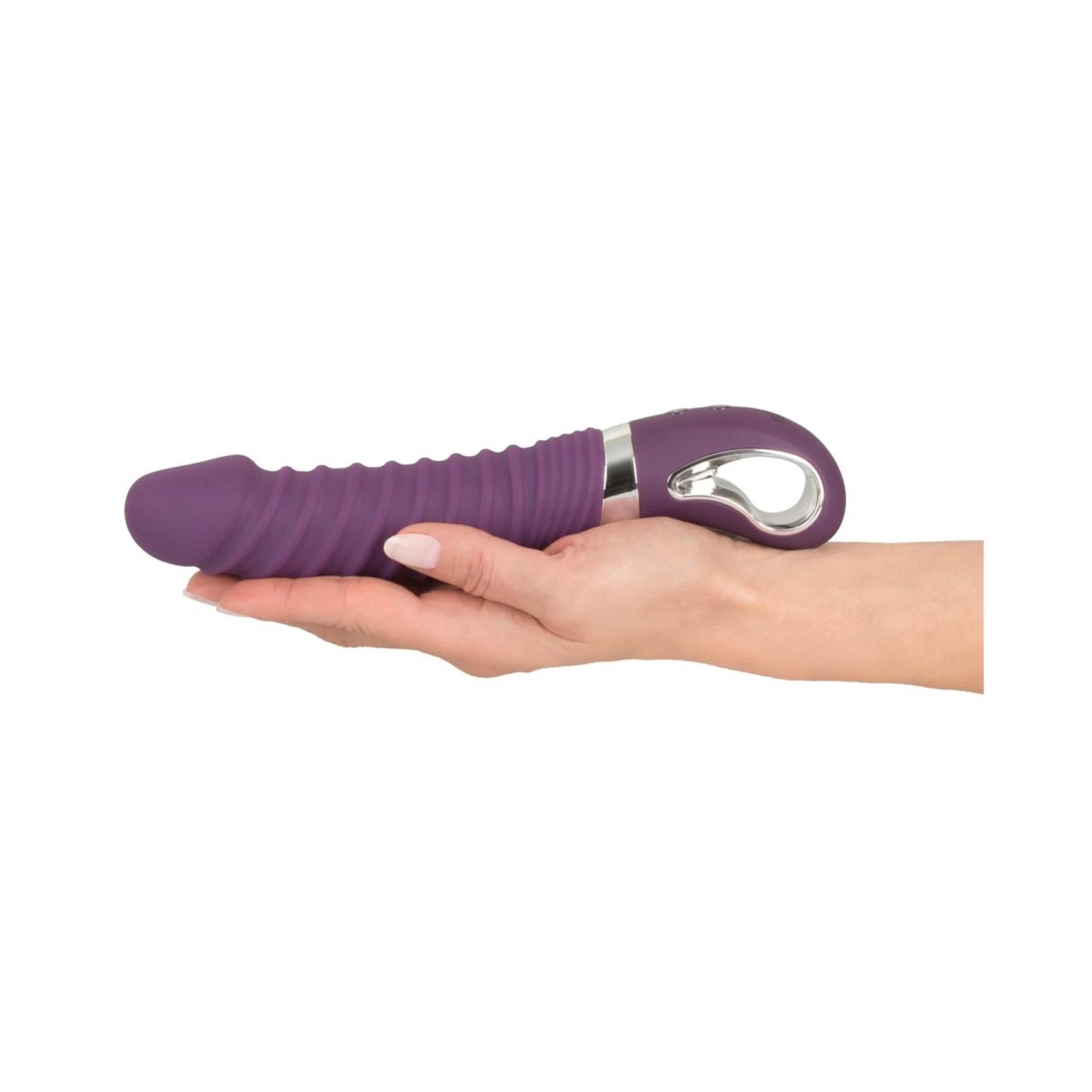 Lila Vibrator in Hand gehalten. Geriffelte Oberfläche, silberfarbener Ring, Bedienfeld. Abgerundete Spitze.