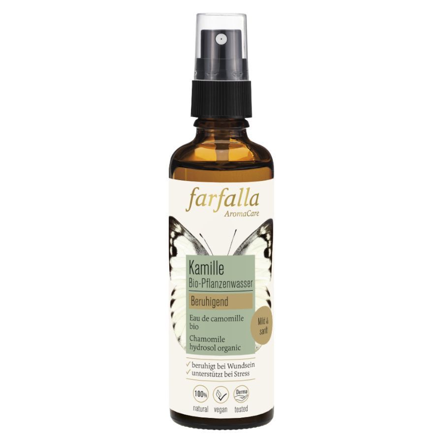 Braune Glasflasche mit Sprühkopf. Etikett mit Produktnamen, Kamille, Bio-Pflanzenwasser, beruhigend. Logos: vegan, natural, Cosmos.