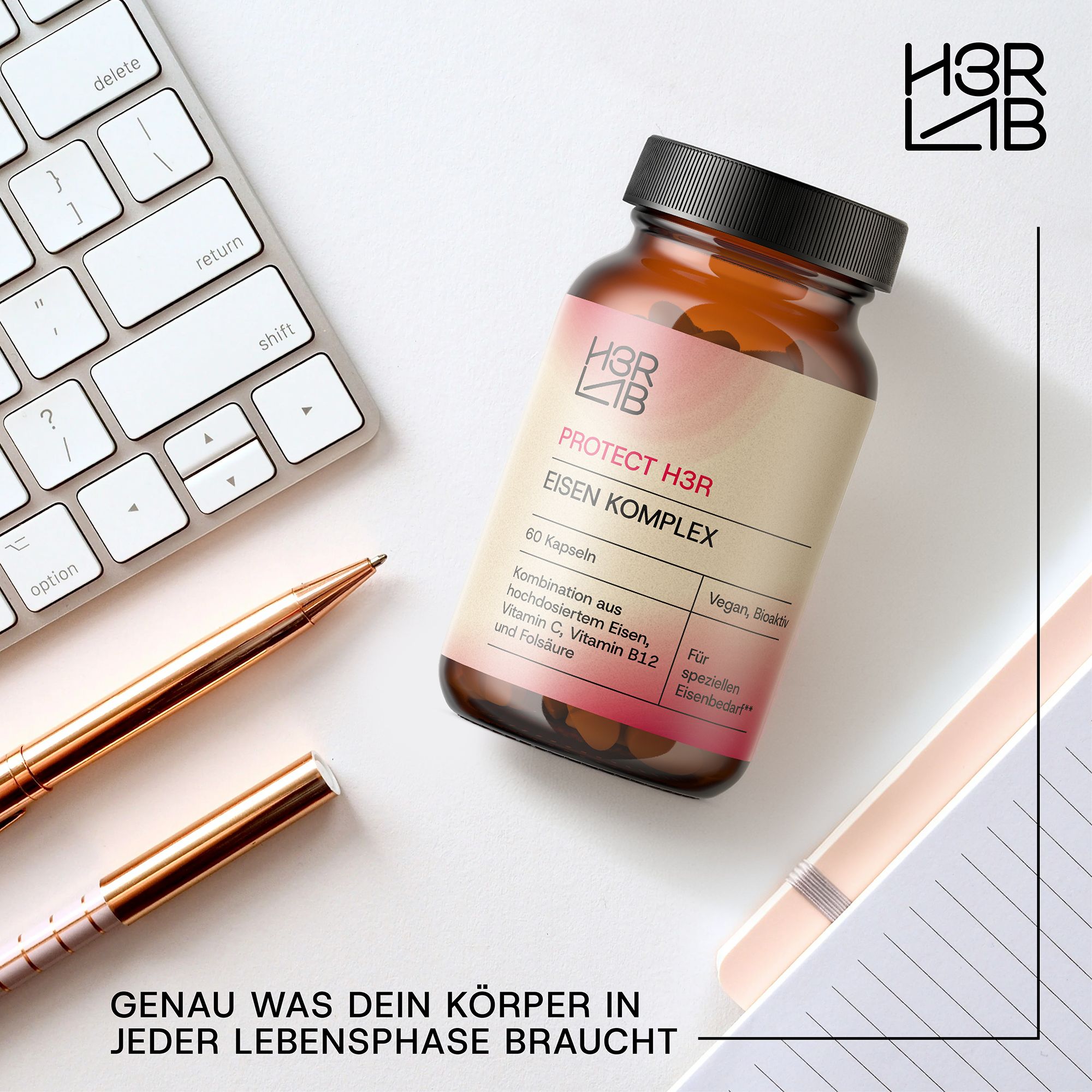 Braune Glasflasche mit schwarzem Deckel. Produktname: Eisen Komplex. Auf Schreibtisch mit Tastatur, Stiften und Notizbuch.