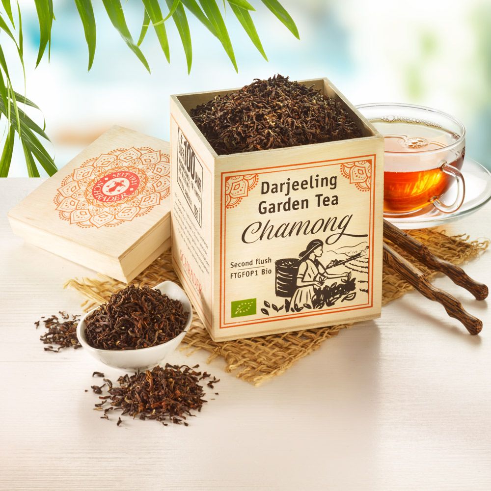 Holzkiste mit losem Tee. Aufschrift: Darjeeling Garden Tea Chamong, Bio-Siegel. Daneben Tasse Tee und Teeblätter.