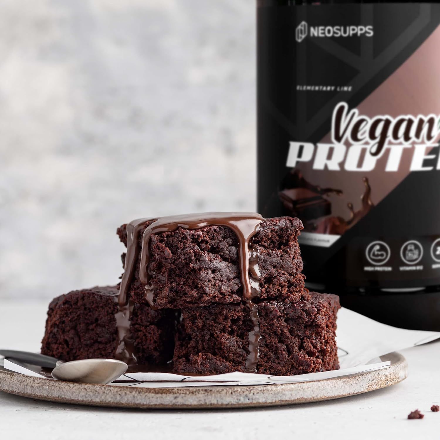 Brownies mit Schokosauce auf Teller. Dose Vegan Protein im Hintergrund. Aufschrift: Neosupps. Braune Dose mit schwarzem Deckel.