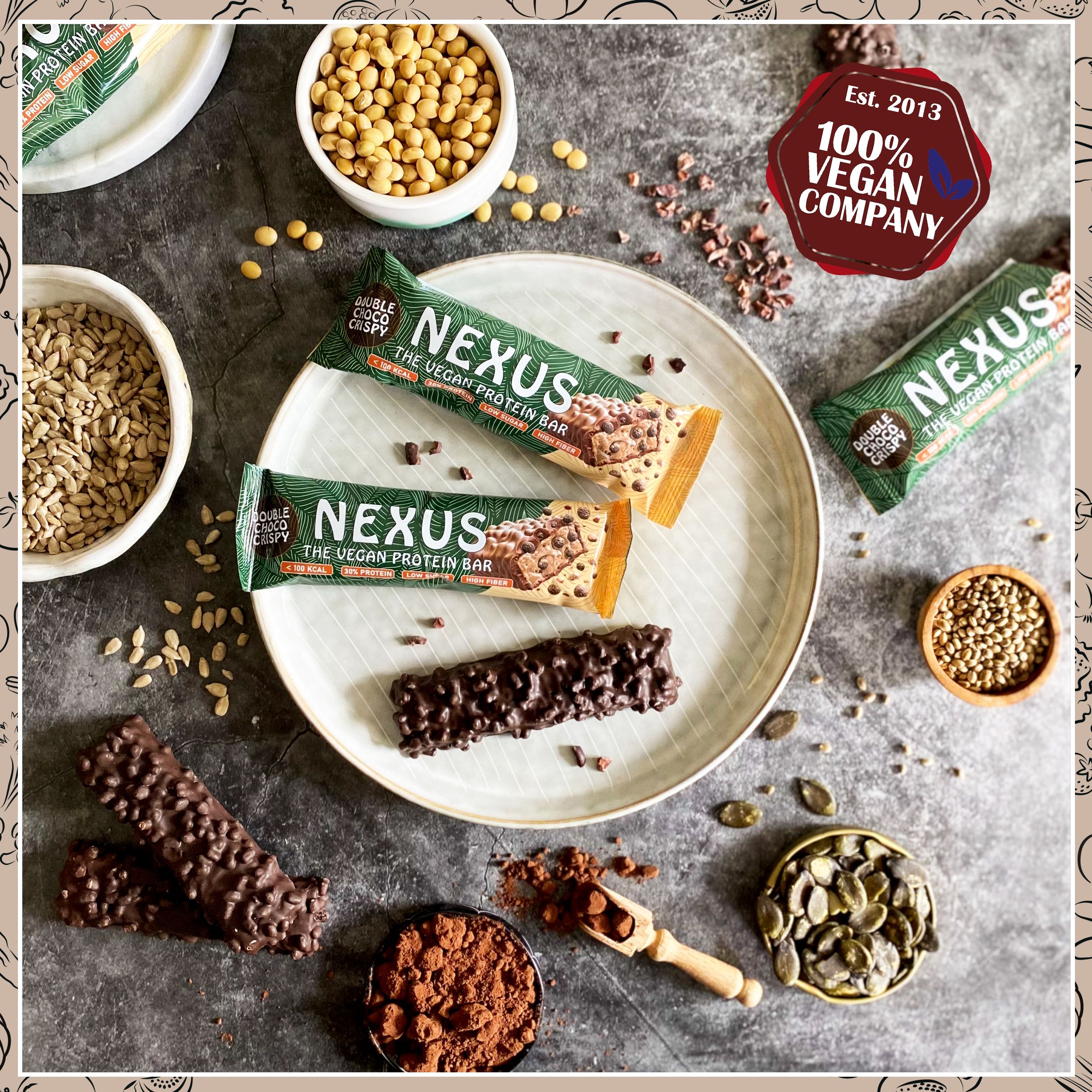 Zwei Nexus Proteinriegel und Zutaten auf einem Teller. Aufdruck: Double Choco Crispy, The Vegan Protein Bar. 100% Vegan Company.