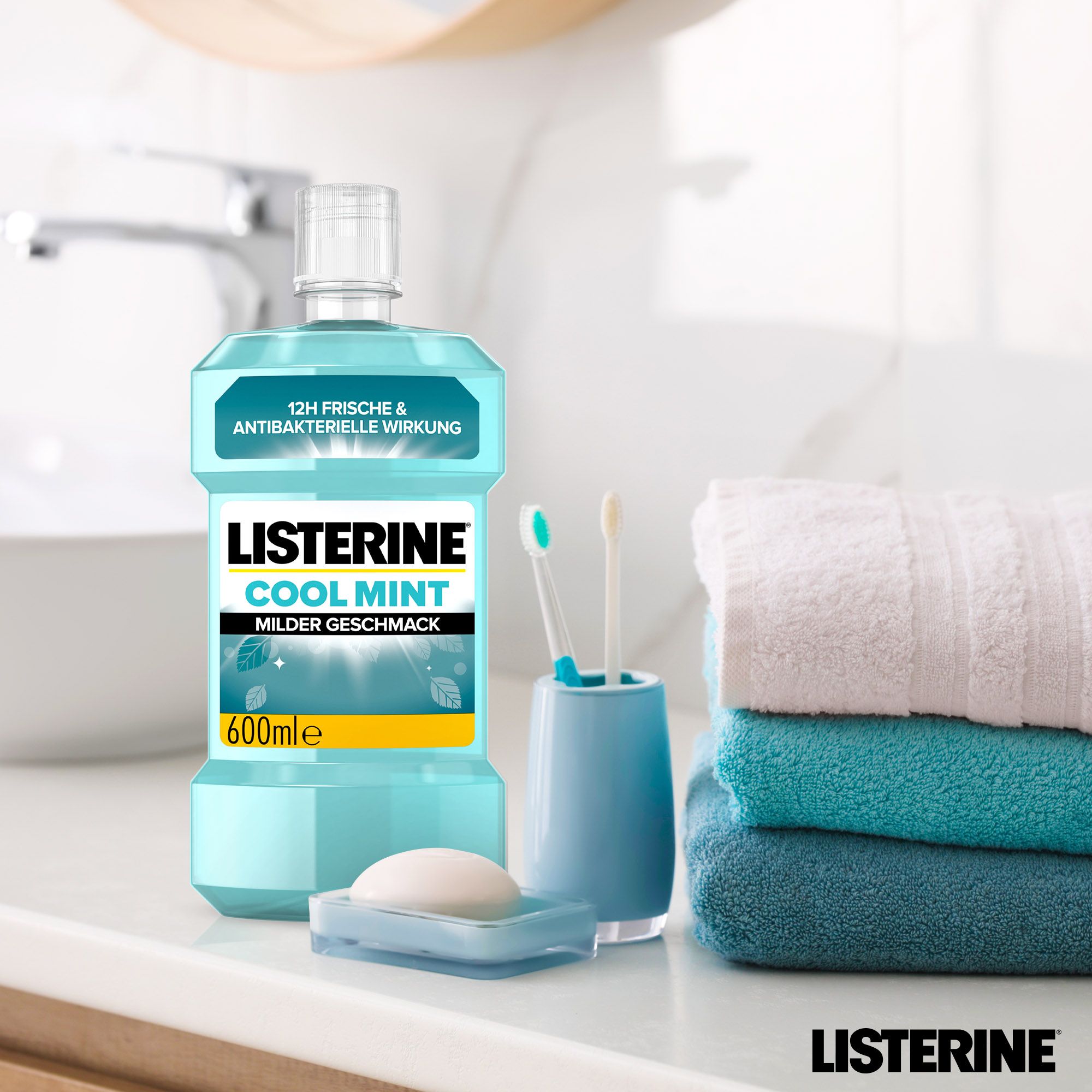 Listerine Cool Mint Mundspülung, blaue Flasche, neben Zahnbürsten, Seife und Handtüchern. Aufschrift: Cool Mint, milder Geschmack.