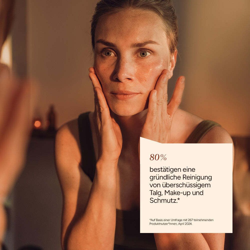 Frau betrachtet ihr Gesicht im Spiegel. Text: 80% bestätigen gründliche Reinigung von überschüssigem Talg, Make-up und Schmutz.