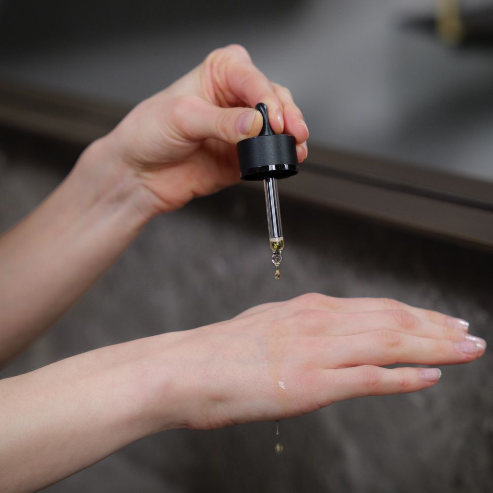 Serum-Pipette tropft auf Hand. Flasche mit schwarzem Deckel. Serum sichtbar.