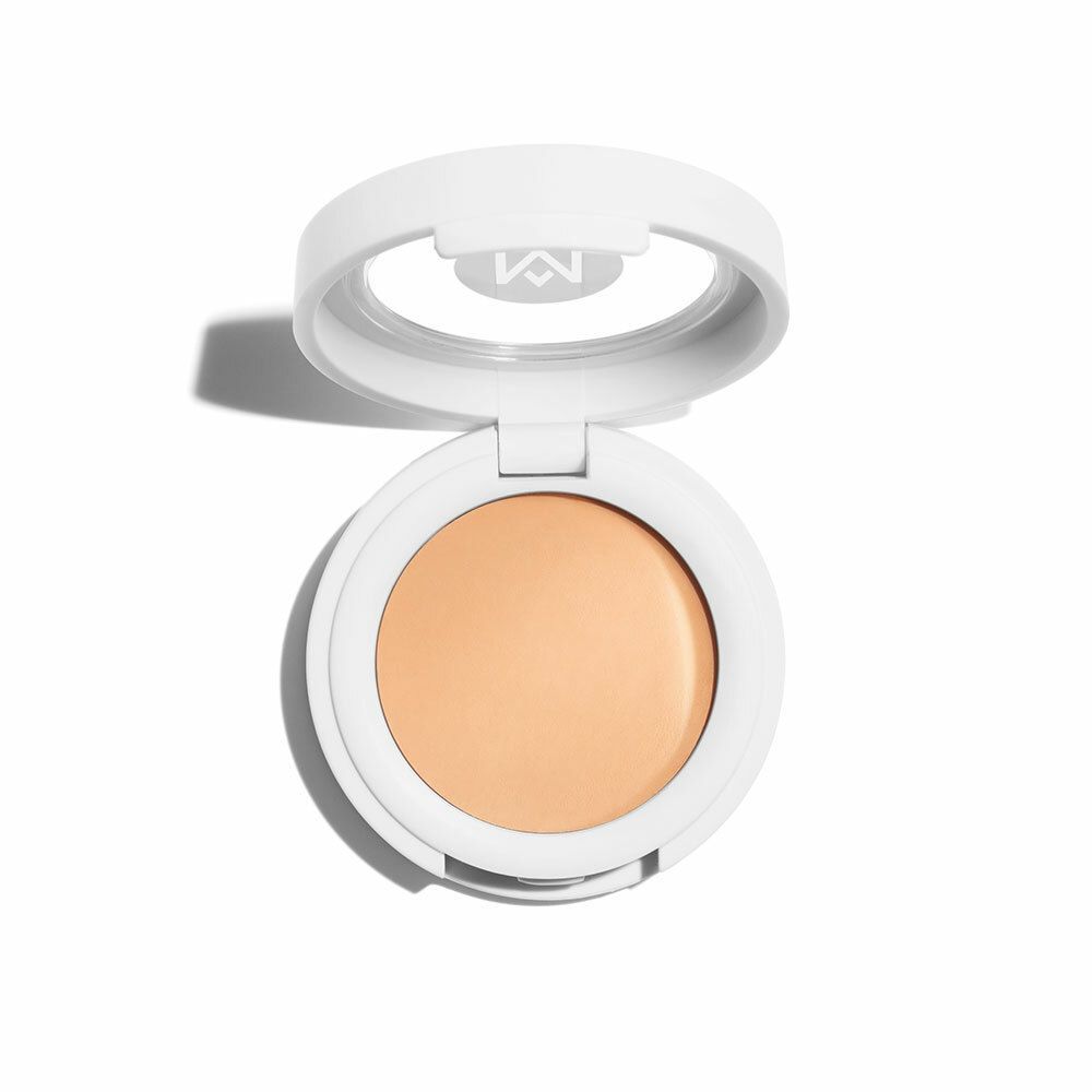 Runder, weißer Concealer-Behälter mit geöffnetem Deckel. Helle, beige Creme im Inneren. Marke mit „M“ im Deckel.