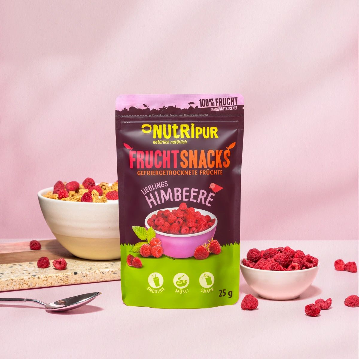 Beutel NutriPur Fruchtsnacks Himbeeren. Daneben Schüssel mit Müsli und Himbeeren. Schüssel mit Himbeeren.
