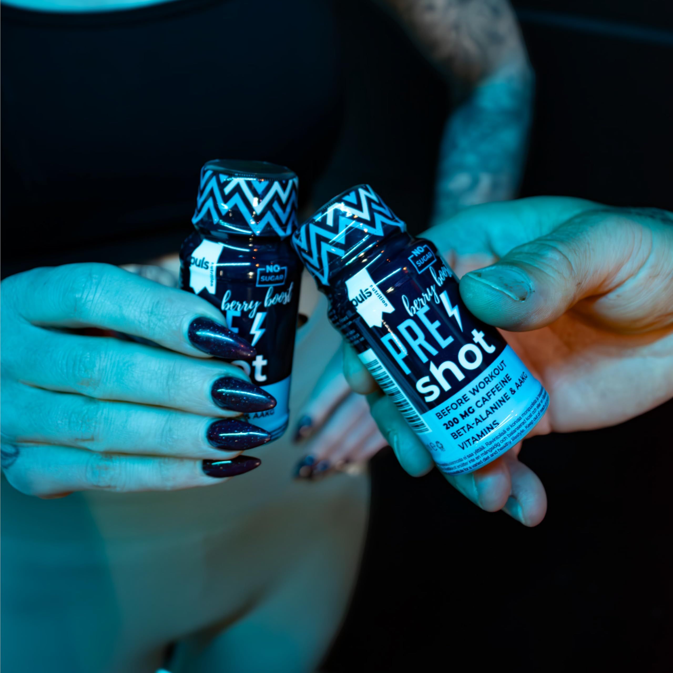 Zwei Hände halten Pre-Workout-Shots mit Beerengeschmack.