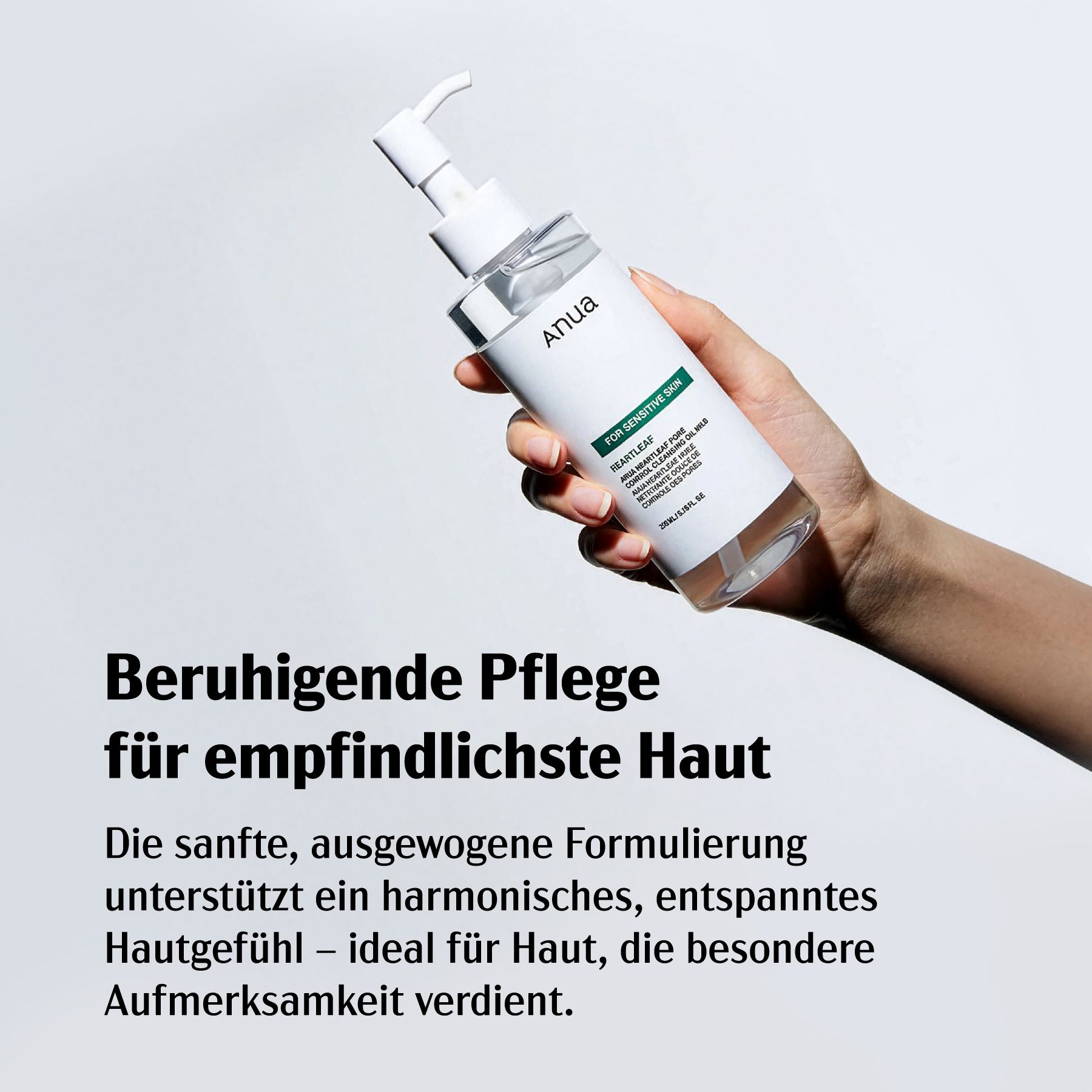 Hand hält Flasche mit weißem Pumpkopf. Text: Anua. Text: FOR SENSITIVE SKIN. Hintergrund grau.
