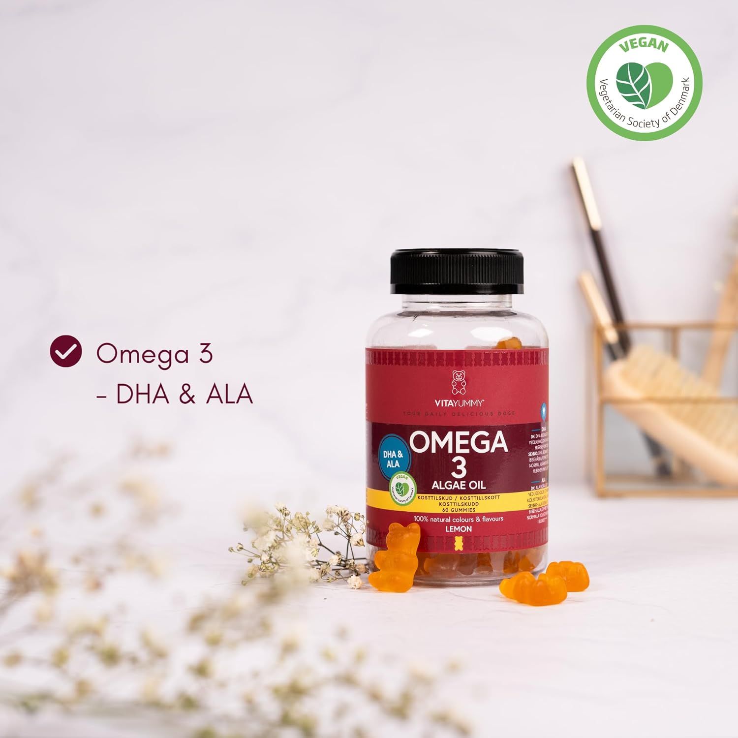 Flasche mit Omega 3 Algenöl Gummibärchen. Aufschrift: VITAYUMMY, Omega 3, Algenöl, Zitrone. Vegan-Siegel. Einige Gummibärchen liegen daneben.