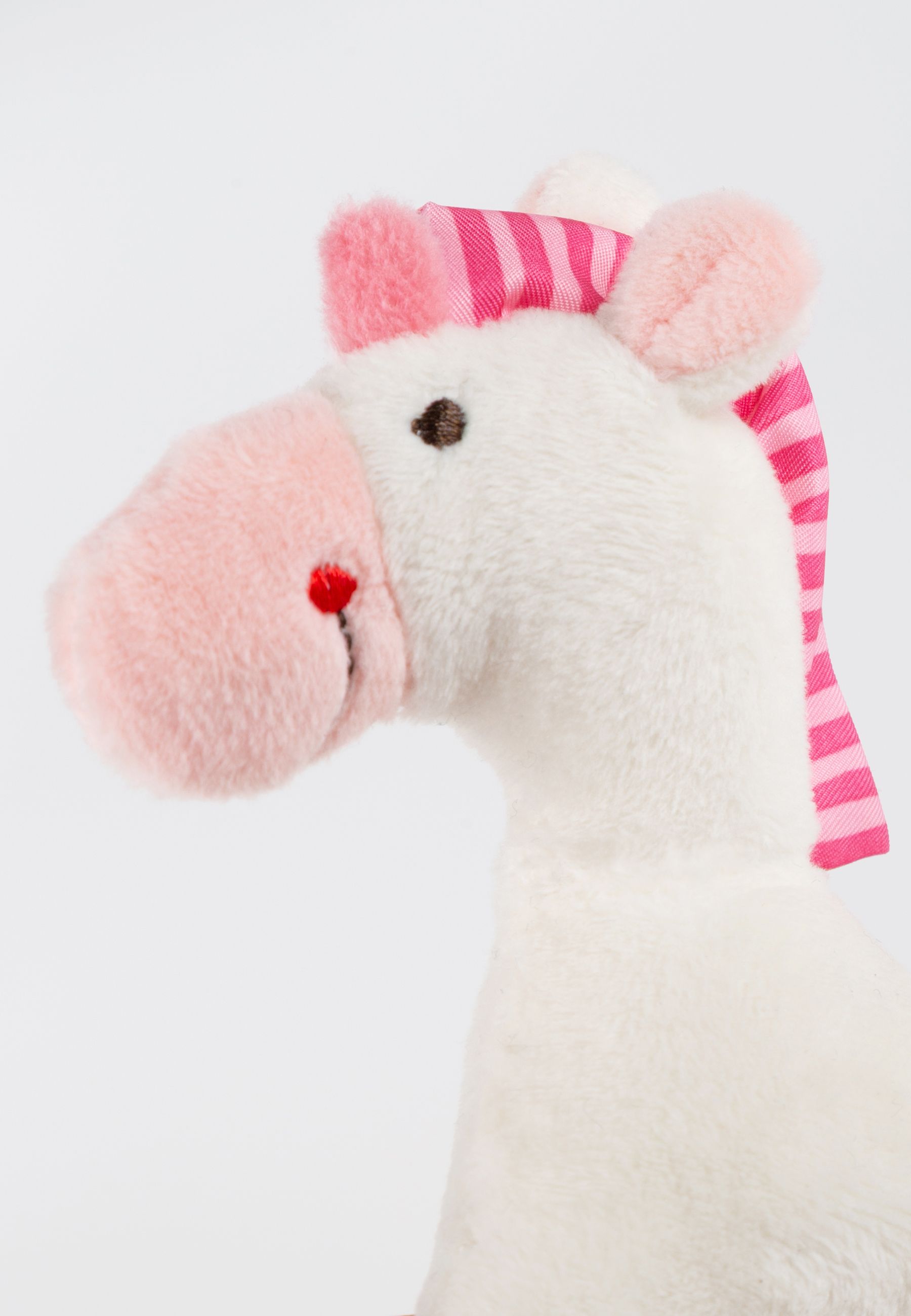 Nahaufnahme eines weißen Stoffeinhorns. Rosa Mähne mit Streifen, rosa Nüstern und Ohren. Roter Punkt auf der Nase.