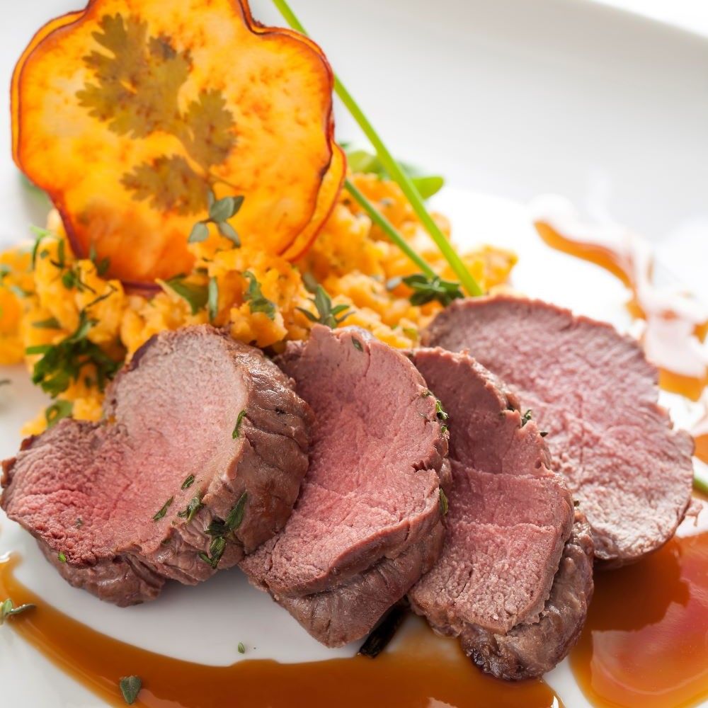Teller mit Fleischscheiben, Gemüse und Soße. Fleisch rosa, Gemüse orange. Weißer Teller.