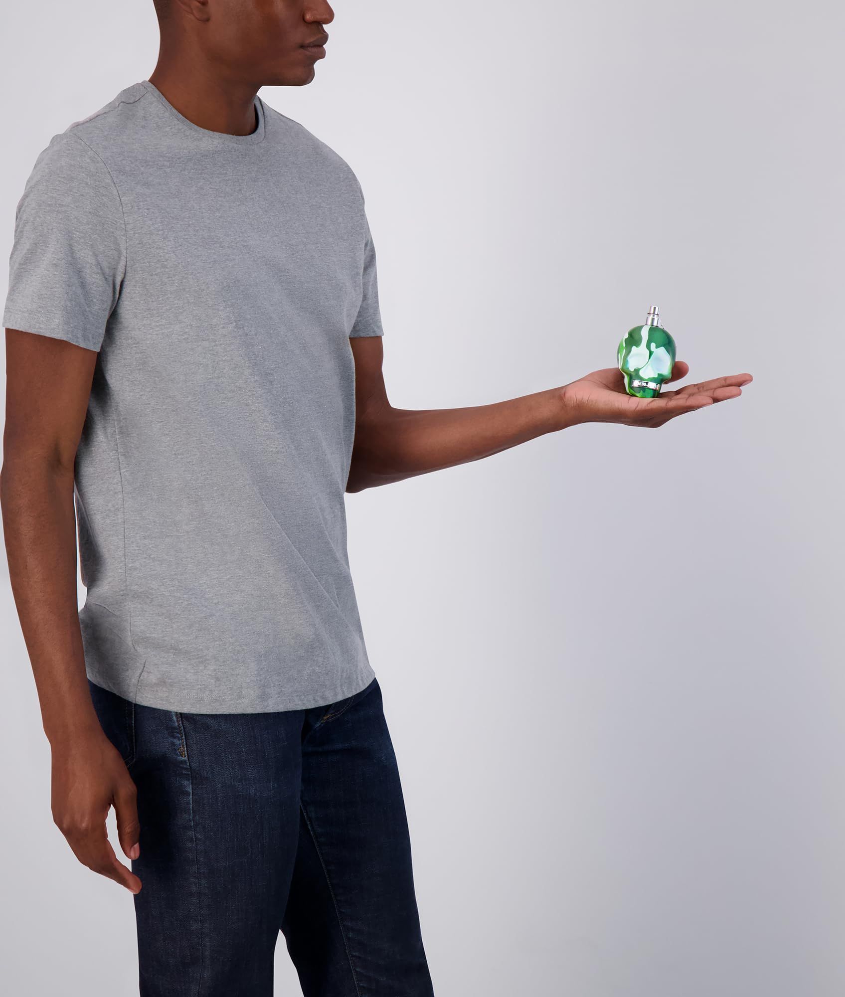 Person hält einen Schädel-Flakon mit Tarnmuster in der Hand. Silberner Zerstäuber.