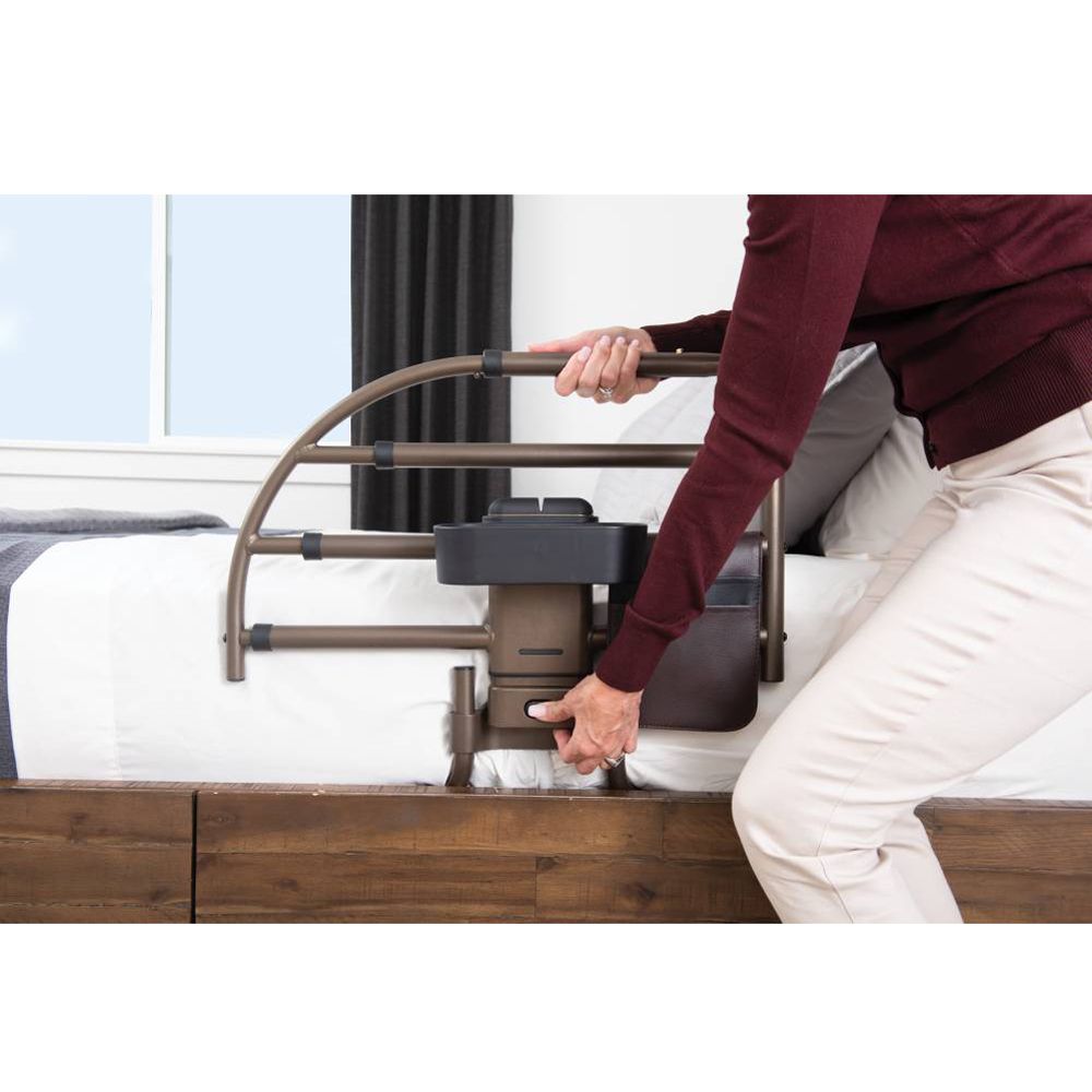 Brauner Bettgriff mit verstellbarem Gestell und schwarzem Motor, an einem Bett montiert.